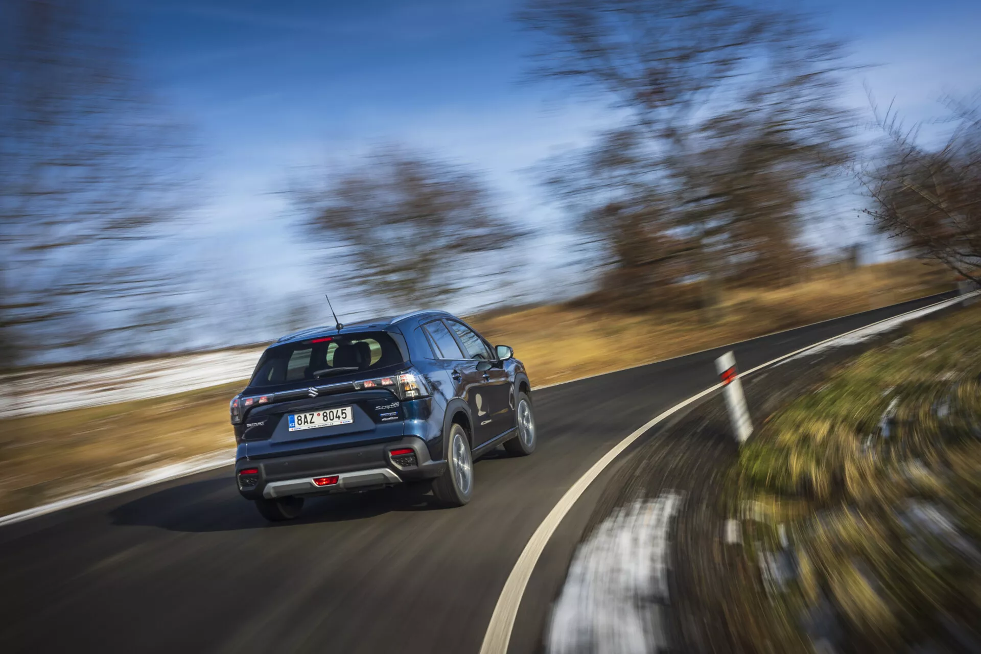 Moderní SUV Suzuki S-Cross 2022 v pohybu, zobrazující profil z pohledu zadní tříčtvrteční části s rotujícími koly na jasný den