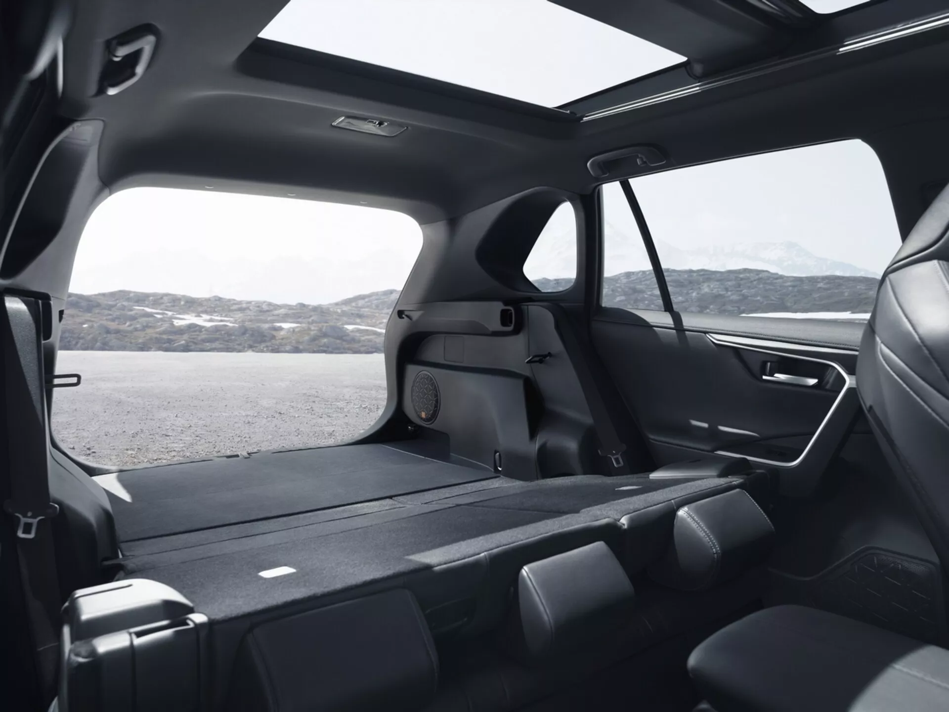 Interiérový pohled na Toyota RAV4 2019 představující prostornou zadní kabinu z vysokého úhlu, zdůrazňující skládací sedadla druhé řady, rozsáhlý nákladový prostor, velká tónovaná okna, moderní design s prémiovými materiály, panoramatické střešní okno, pokročilé osvětlení a funkce klimatizace