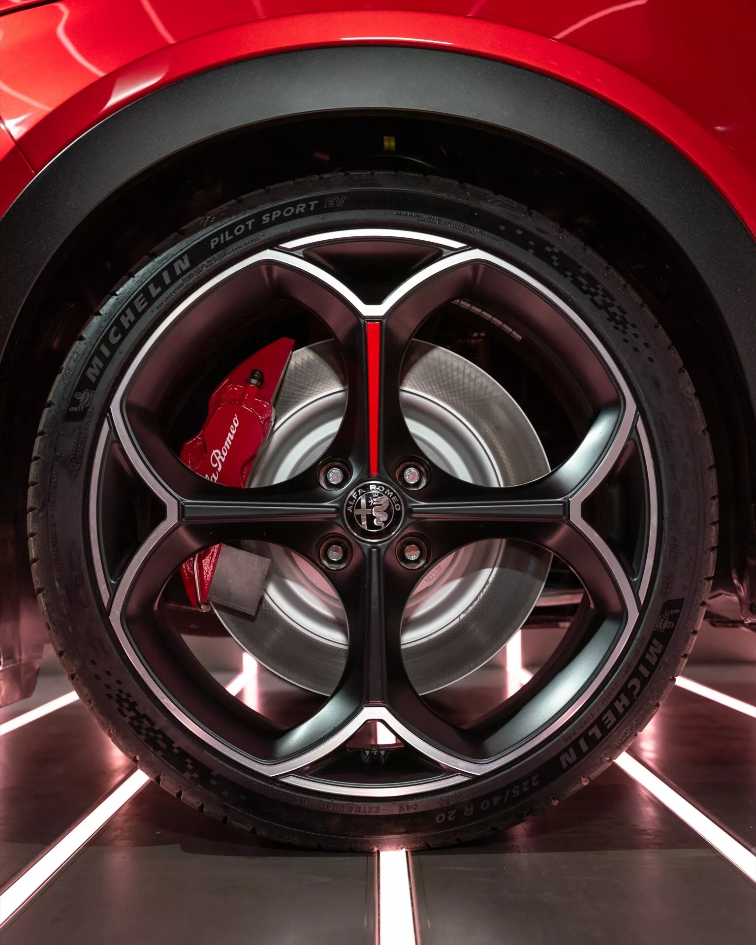 Detailní pohled na kolo Alfa Romeo Junior 2024 s propracovaným designem ráfku a pneumatikou Michelin Pilot Sport 4 v prostředí showroomu, zdůrazňující výkon a sportovní estetiku