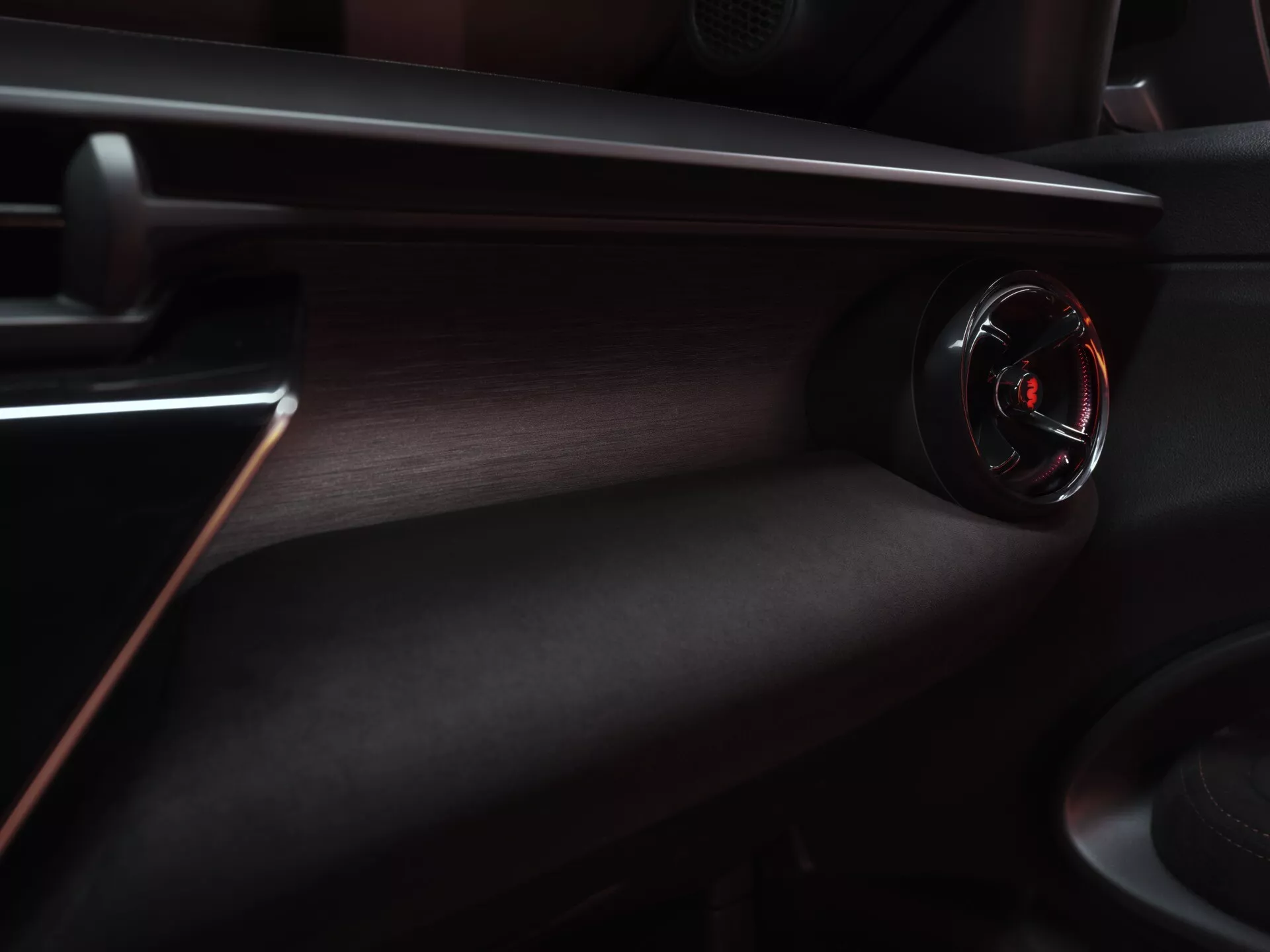 Interiérový pohled na Alfa Romeo Junior 2024, zdůrazňující palubní desku na straně spolujezdce s kruhovým větracím otvorem s lesklým černým povrchem a červeným akcentem, obklopeným luxusní tmavě texturovanou palubní deskou s červeným dekorativním prošíváním
