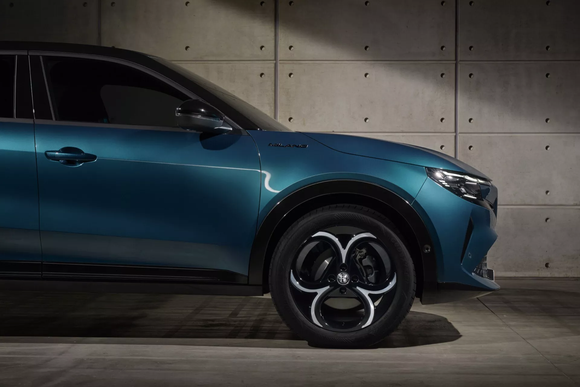 Pohled z nízkého úhlu na Alfa-Romeo Junior (966) rok 2024 s důrazem na boční profil, včetně odznaku TurboS, vysokovýkonných brzd, složitého designu ráfku a elegantního metalického modrého laku