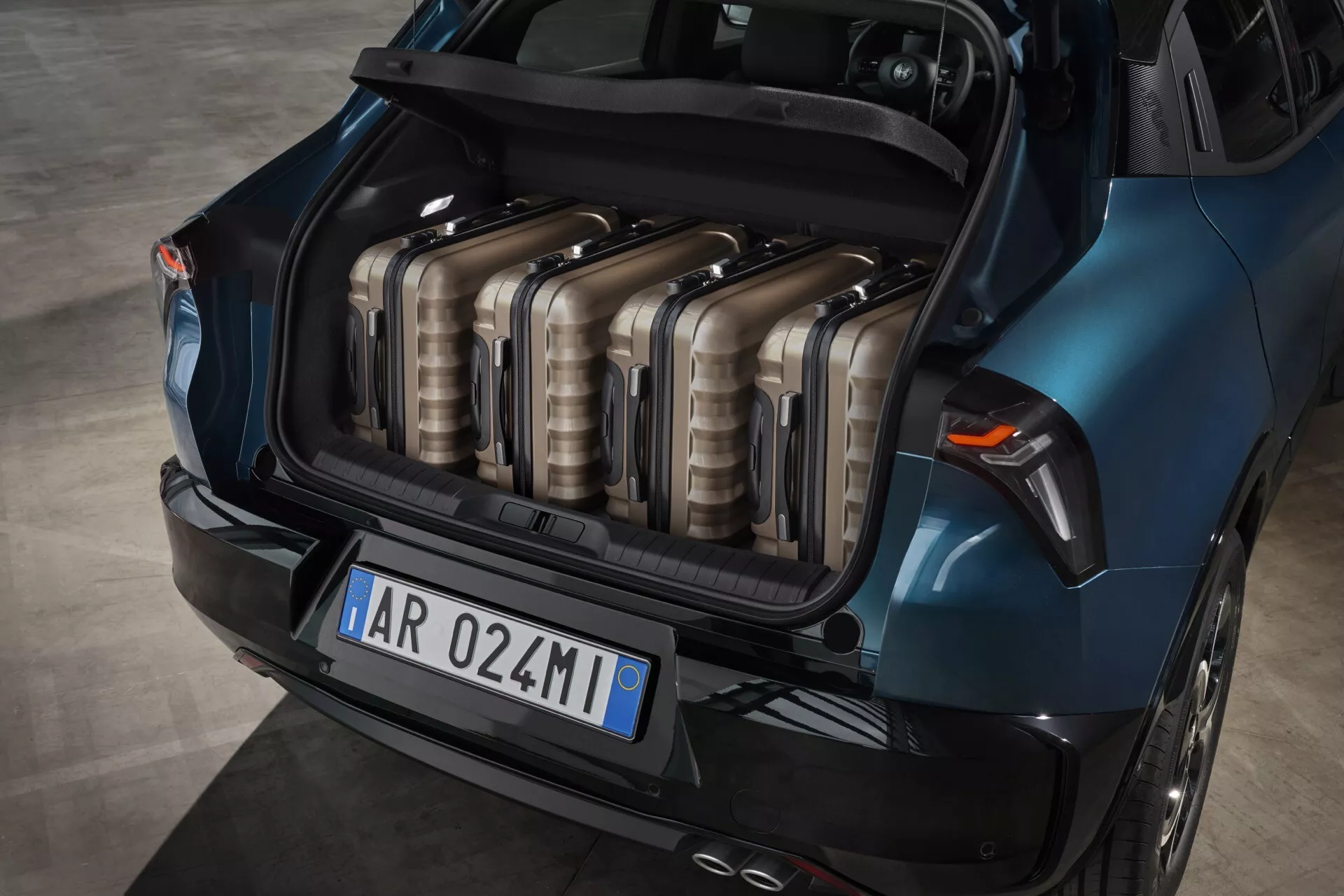 Alfa-Romeo Junior 966 z roku 2024 prezentuje svůj prostorný modrý kufr z vysokého úhlu, ukazuje uspořádání zavazadel a designové prvky včetně tvaru zadních světel a zakřivení zadního nárazníku.