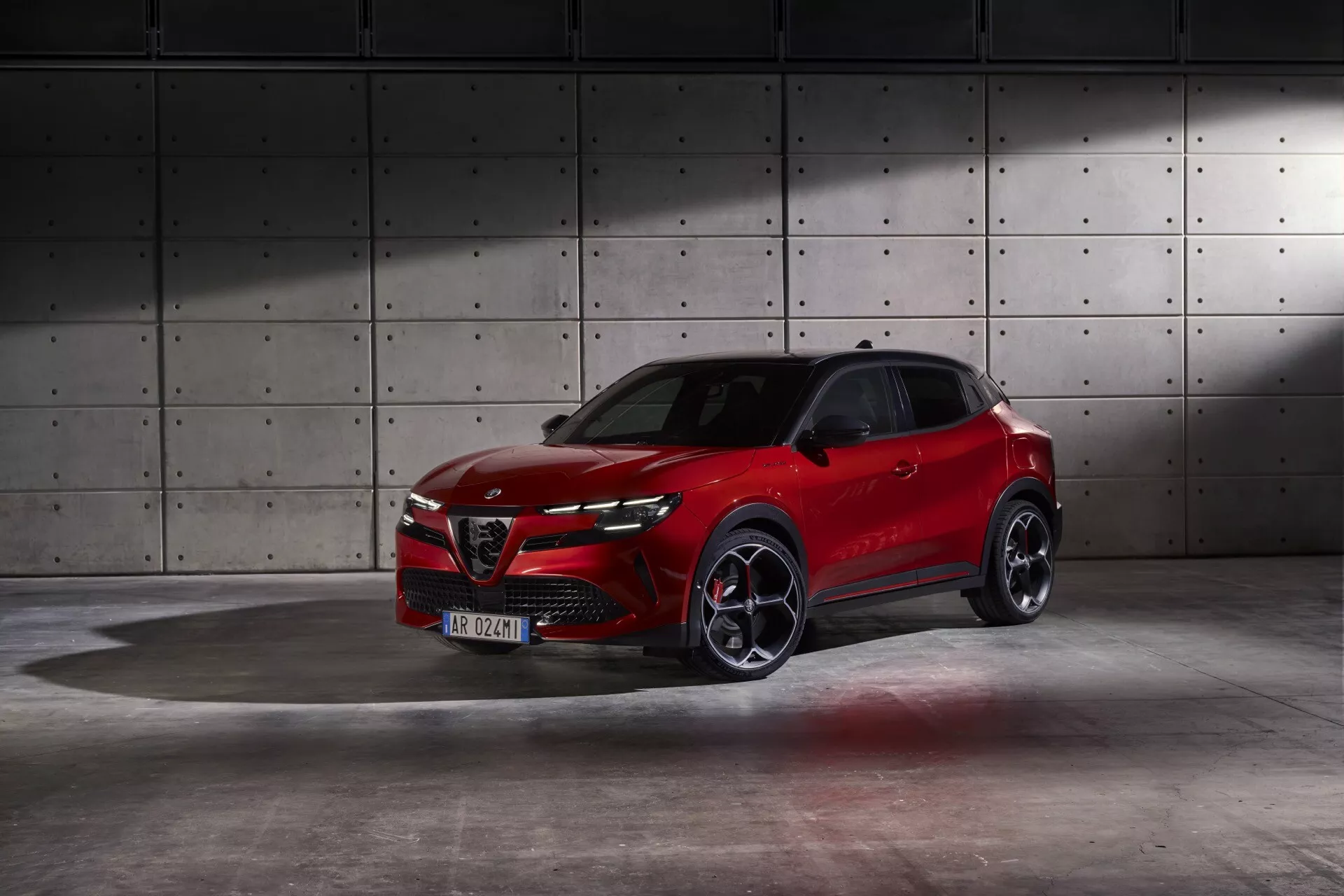 Alfa Romeo Junior 966 ročník 2024 v jasně červené barvě předvádějící dynamický design a pokročilé funkce v profesionálním studiovém prostředí s industriálním pozadím