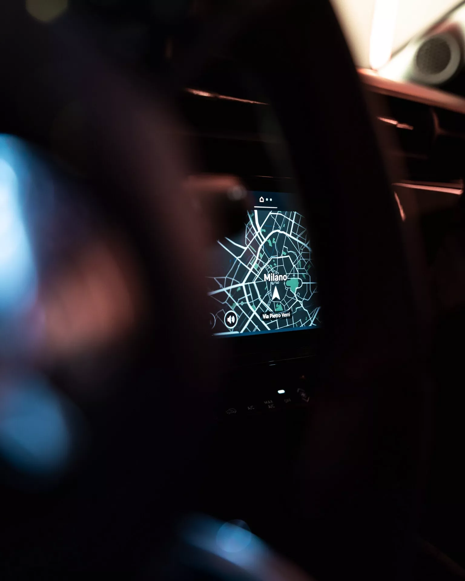Pohled z interiéru na infotainment systém Alfa Romeo Junior 2024 zobrazující GPS mapu Milána s navigačními ikonami, z pohledu řidiče s malou hloubkou ostrosti