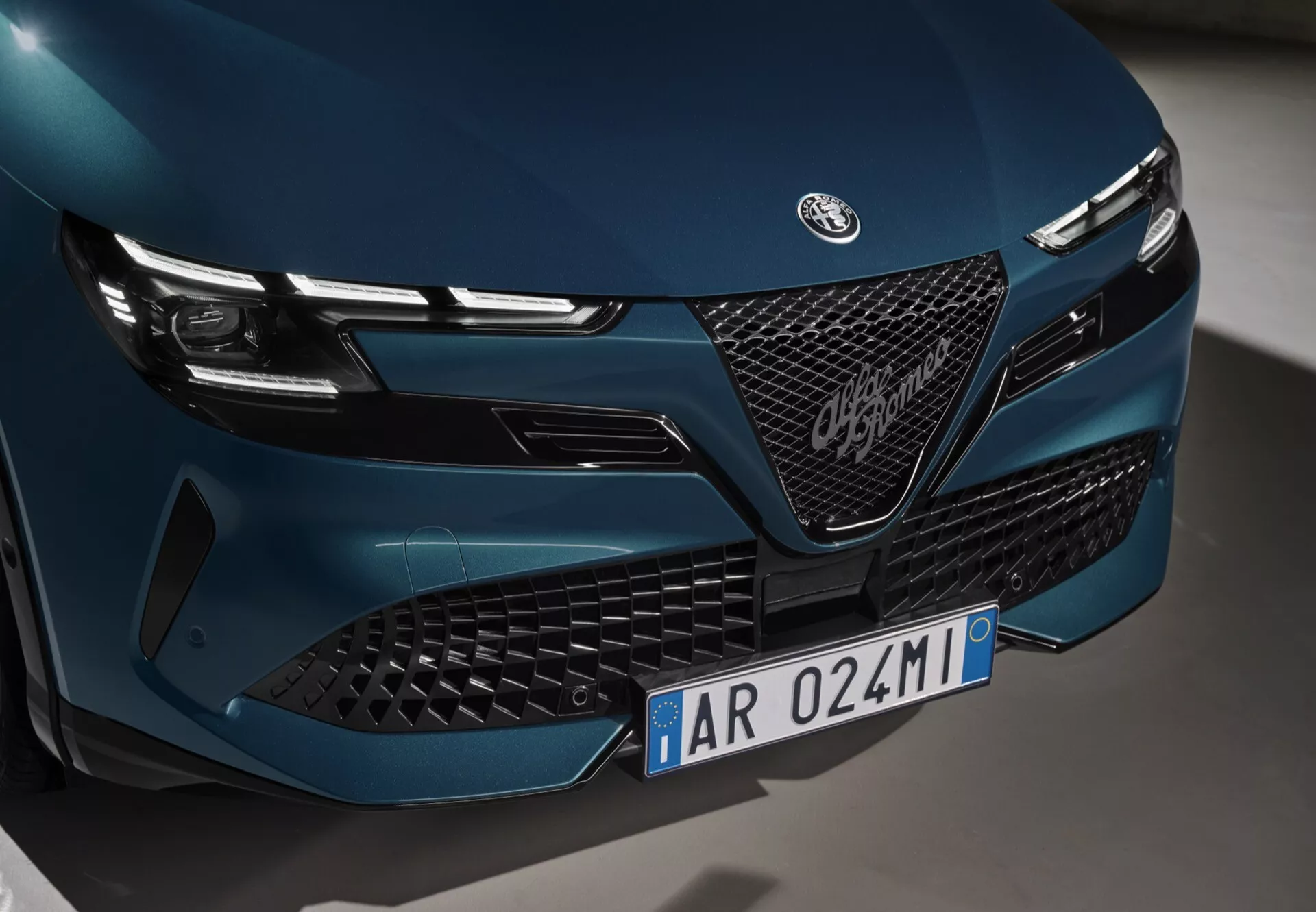 Detailní pohled na přední část Alfa-Romeo Junior 2024 s důrazem na mřížku, emblém a LED světlomety s elegantním a agresivním designem, snímek z nízkého úhlu z levé strany
