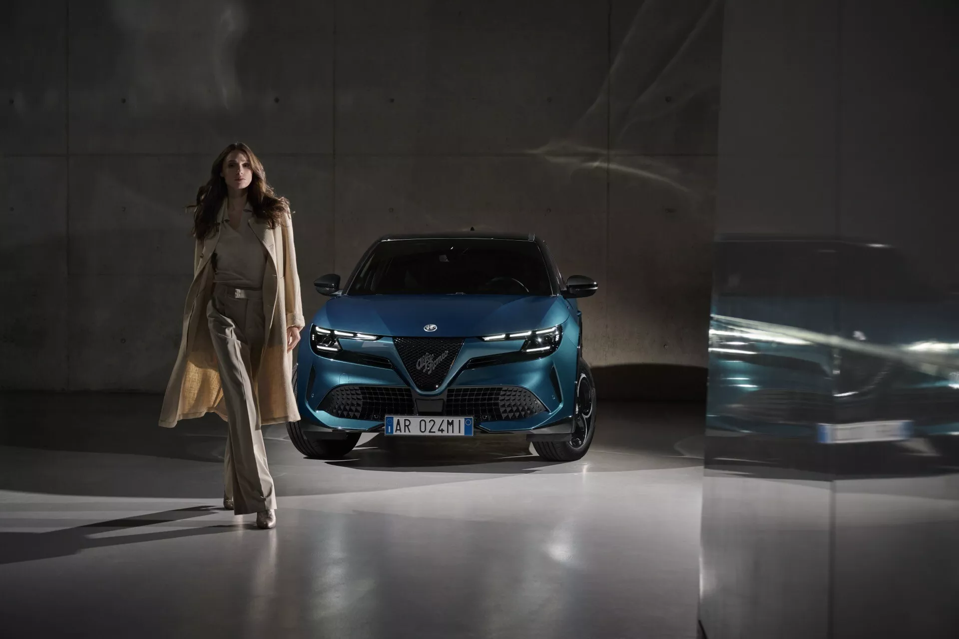 Alfa-Romeo Junior 2024 fotografované z nízkého předního úhlu, které zdůrazňuje mřížku, LED světlomety a moderní přední část vozu v tmavě metalické modré, zdůrazňuje pokročilou technologii osvětlení a design v městském prostředí