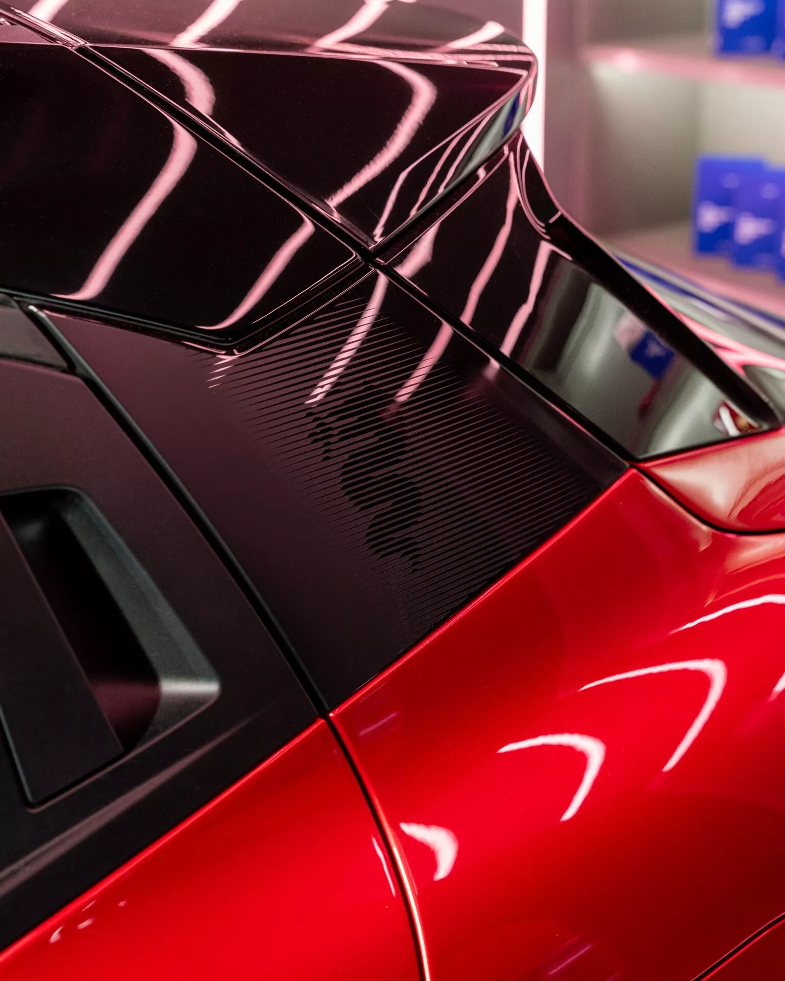 Detailní pohled na zadní část Alfa-Romeo Junior 2024 s sportovním červeným provedením, integrovaným spoilerem, detaily z karbonových vláken a designem zadního okna odrážejícím složité světelné vzory.