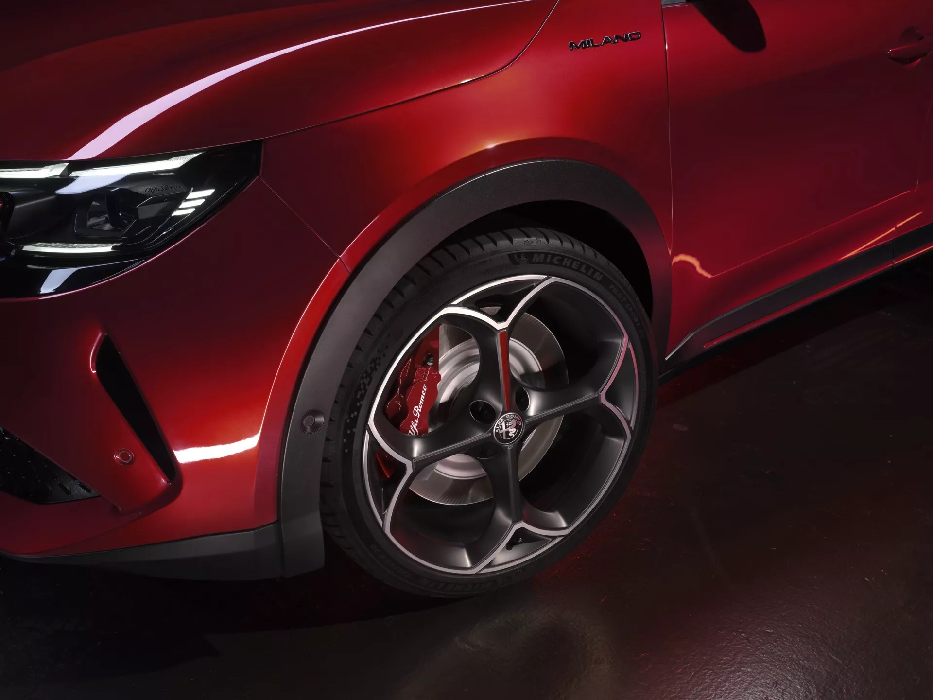 Detailní pohled na přední levé kolo a blatník Alfa Romeo Junior 2024, předvádějící vícepaprskové slitinové ráfky, lesklý červený lak a červený brzdový třmen pro prémiový a na výkon orientovaný vzhled