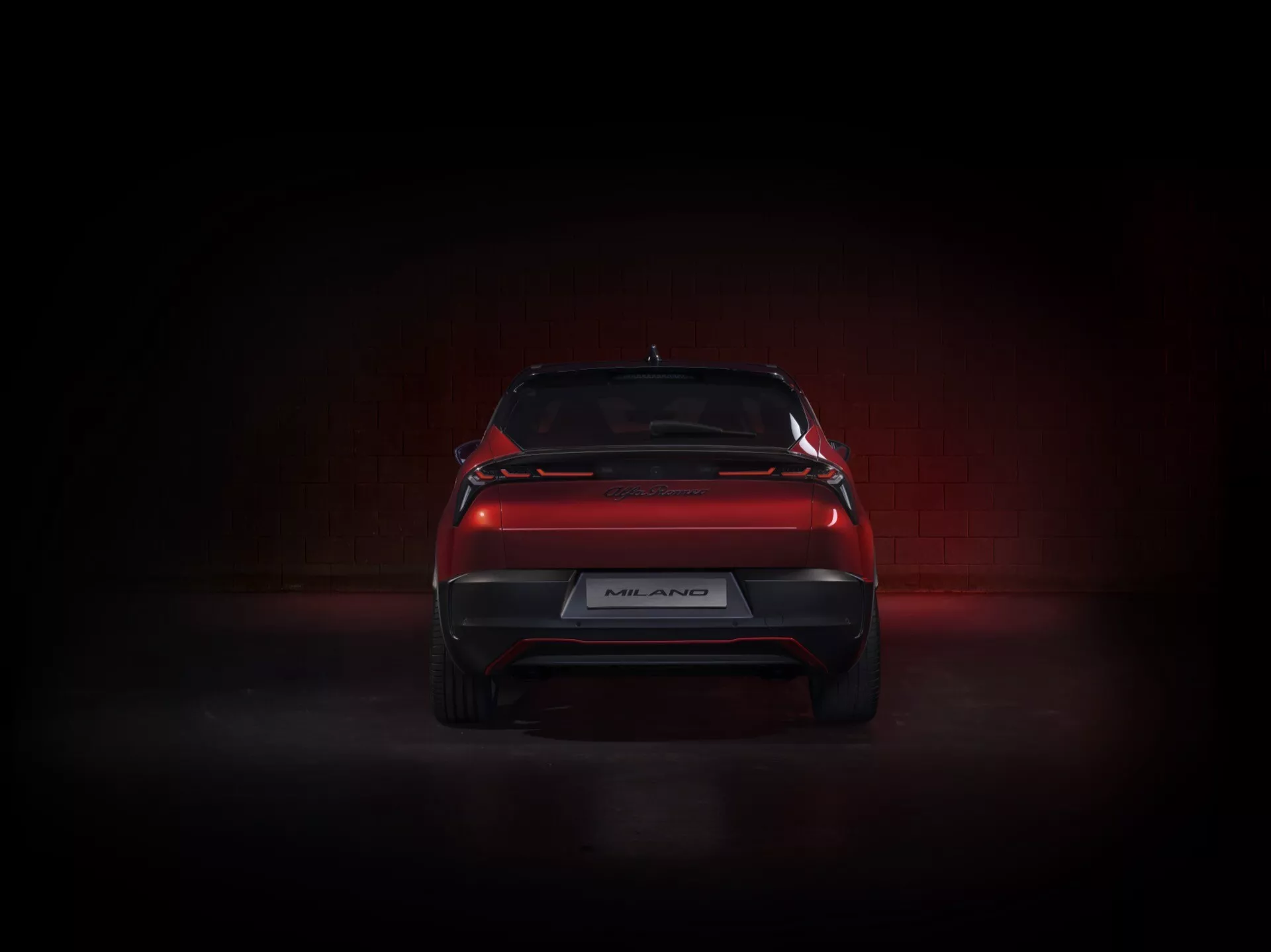 Zadní pohled na Alfa Romeo Junior 2024 s elegantním designem, LED zadními světly, sportovním zadním difuzorem a spoilerem kufru ve dramatickém osvětlení studia