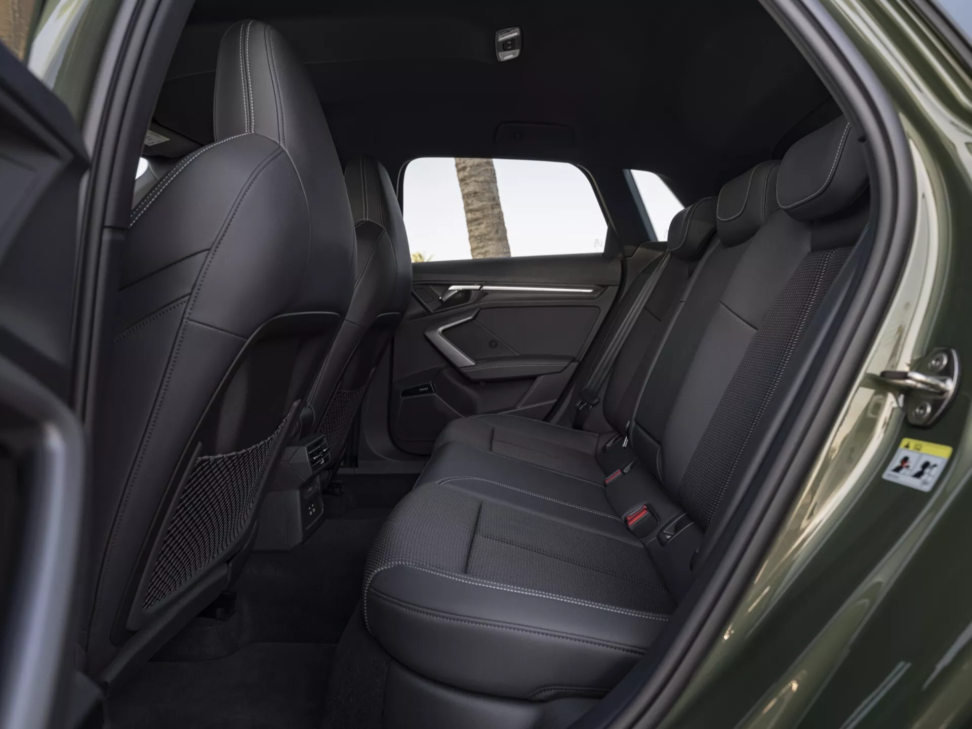 Interiér zadní části Audi A3 8Y facelift z roku 2024 z boční perspektivy, zdůrazňující sedadla z černé kůže, ovládání elektrických oken, zadní klimatizační výdechy a centrální konzolové technologie