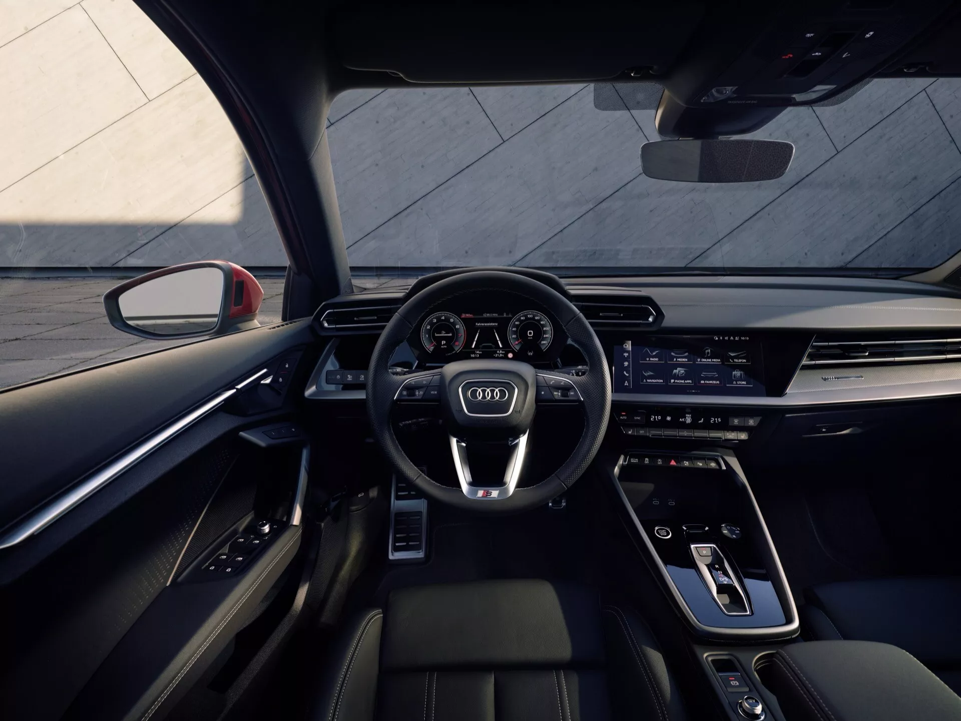 Vnitřní pohled na Audi A3 2024 (8Y-Facelift) z pohledu řidiče z zadní lavice, s sportovním volantem s multifunkčními tlačítky, prodlouženým digitálním palubním a infotainmentovým displejem, elegantní středovou konzolou s minimem fyzických ovládacích prvků, moderními předními sedadly s prémiovými materiály a kontrastním prošíváním a ambientním osvětlením.