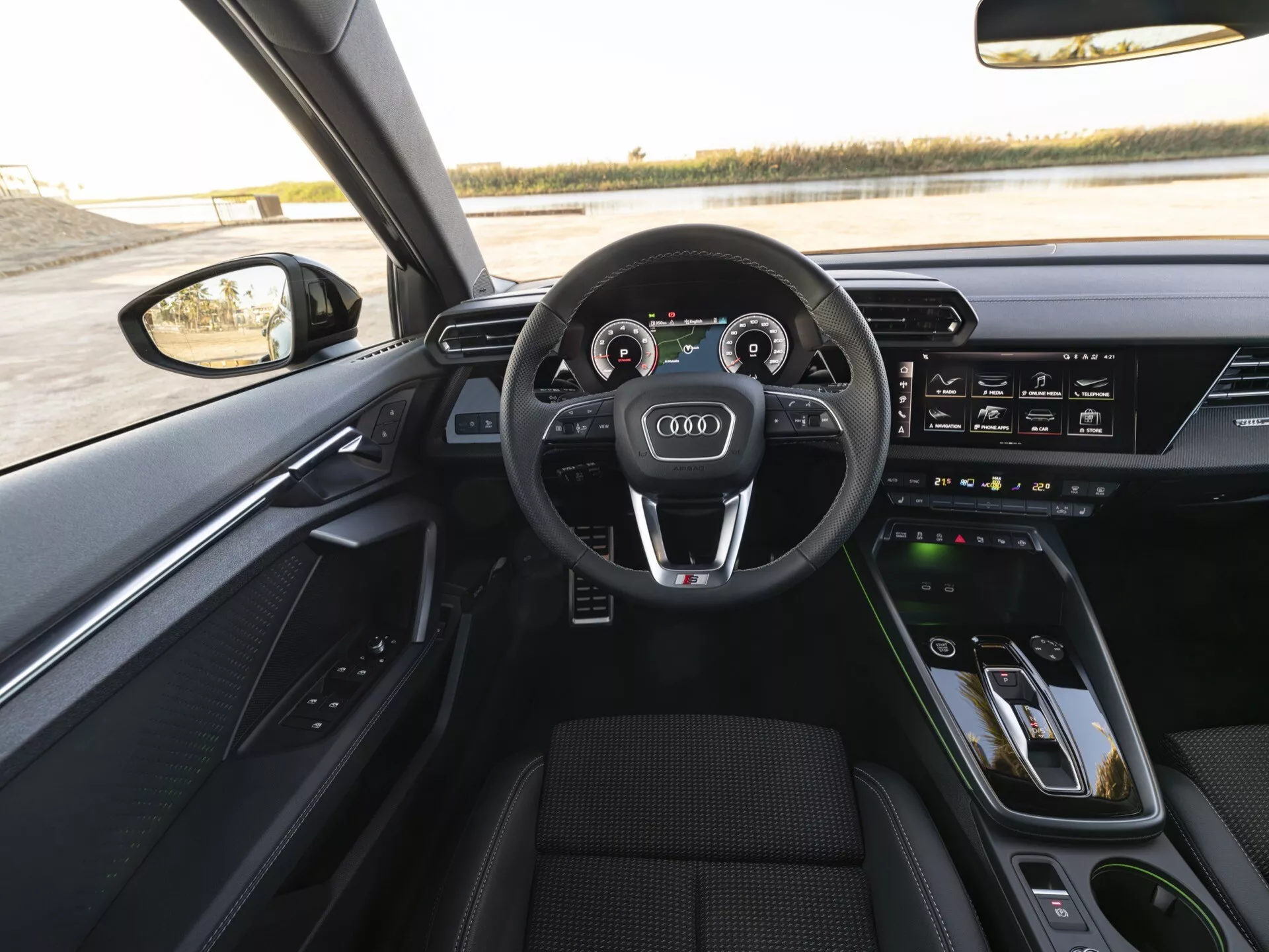 Interiérový pohled z perspektivy řidiče na Audi A3 2024 (8Y-Facelift), ukazující tříramenný volant potažený kůží s multifunkčními tlačítky, digitální přístrojový panel známý jako Audi Virtual Cockpit, dotykový displej MMI na středové konzole, ovládání klimatizace a ovládání prémiového audiosystému na dveřích řidiče.