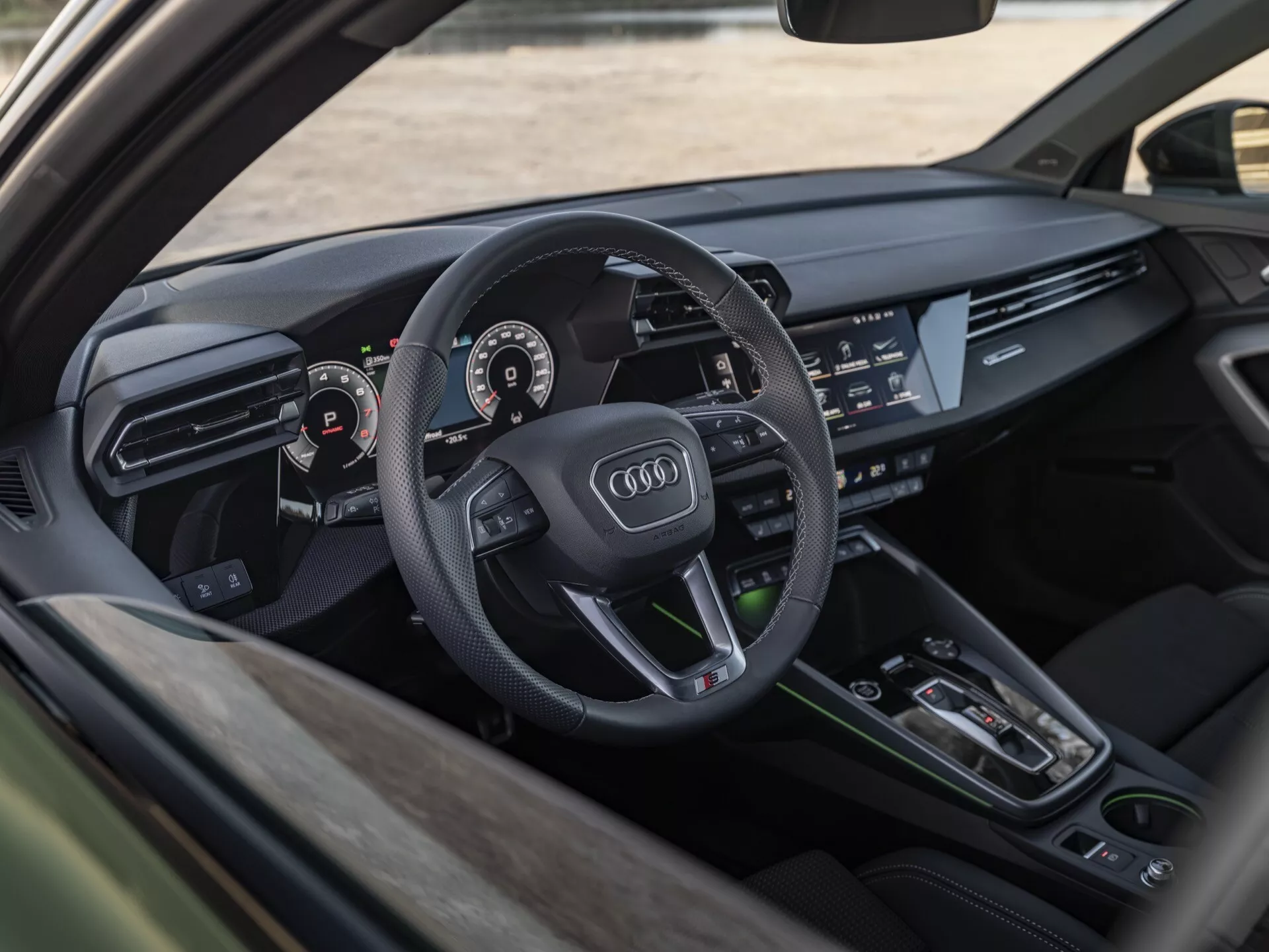 Interiérový pohled na Audi A3 2024 (8Y-facelift) zobrazující stranu řidiče s detailním záběrem palubní desky, volantu s emblémem Audi, digitálního přístrojového panelu a informačně-zábavního systému