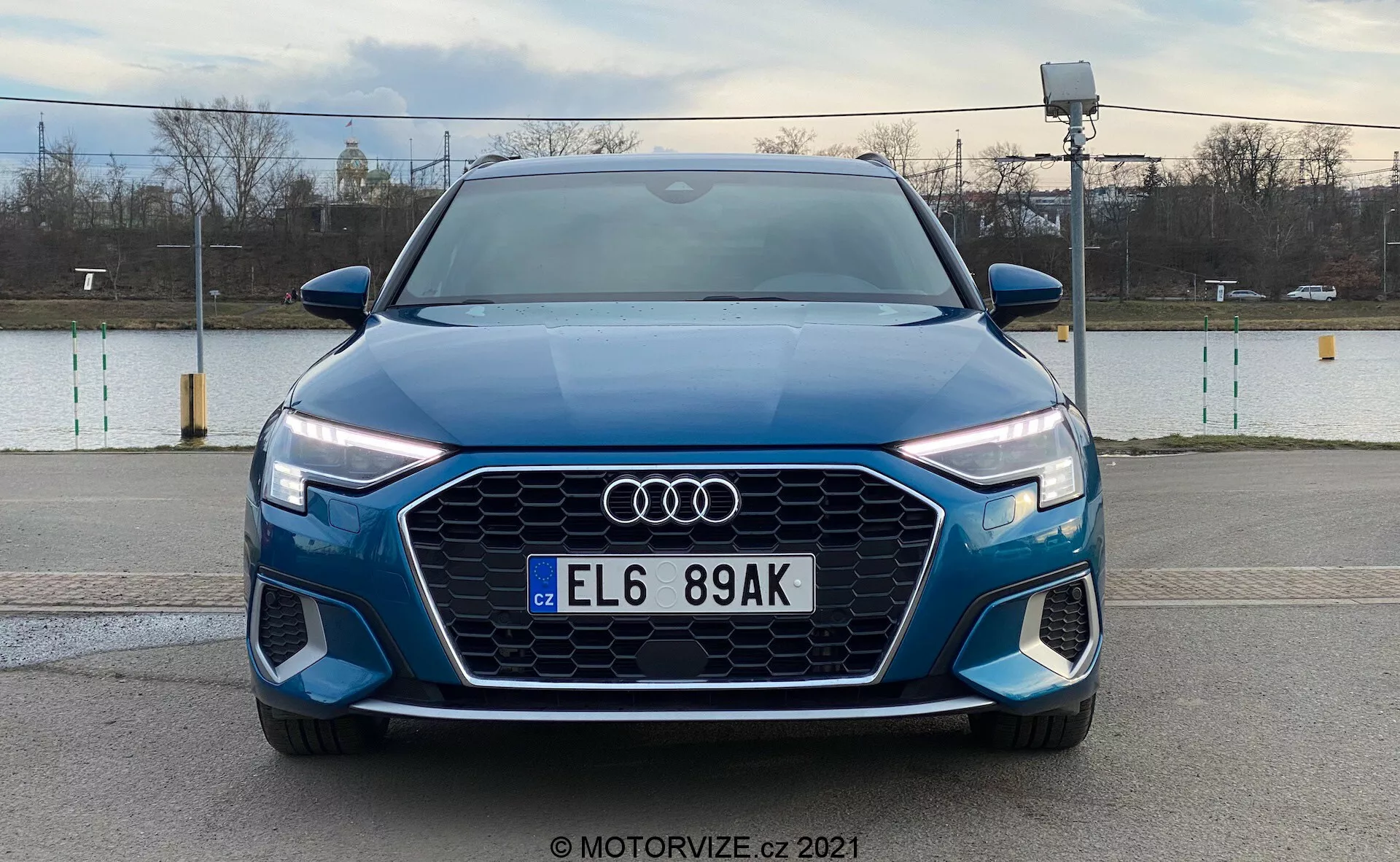 Čelní pohled na modrý Audi A3 Sportback 2020, který se chlubí výraznou maskou Singleframe s hexagonálním designem, logem Audi uprostřed, LED světlomety s denním svícením a předním nárazníkem s dalšími vzduchovými otvory a možnými mlhovými světly, na pozadí venkovního prostředí.