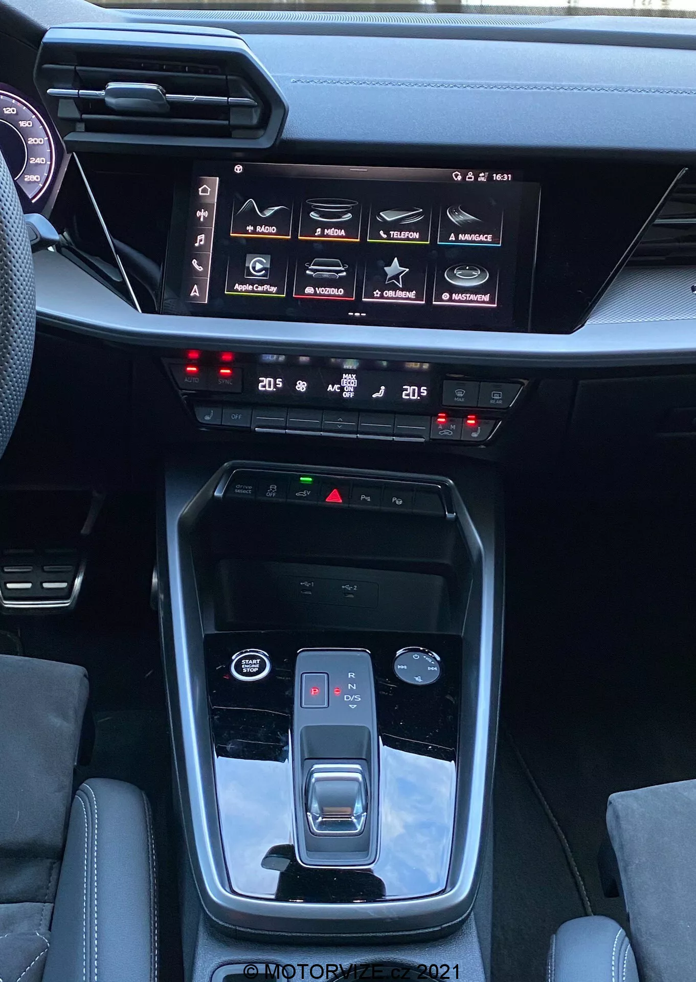 Interiér Audi A3 2020 Sportback s přehlídkou středové konzole a přístrojové desky, zdůrazňuje funkce jako automatická převodovka s tlačítkem parkování, elektronická parkovací brzda, volič jízdních režimů, kovové akcenty, dotykový infotainment systém s různými nastaveními vozidla, dvouzónový klimatizační systém, tlačítka bezpečnostních funkcí a elegantní, moderní design přístrojové desky.