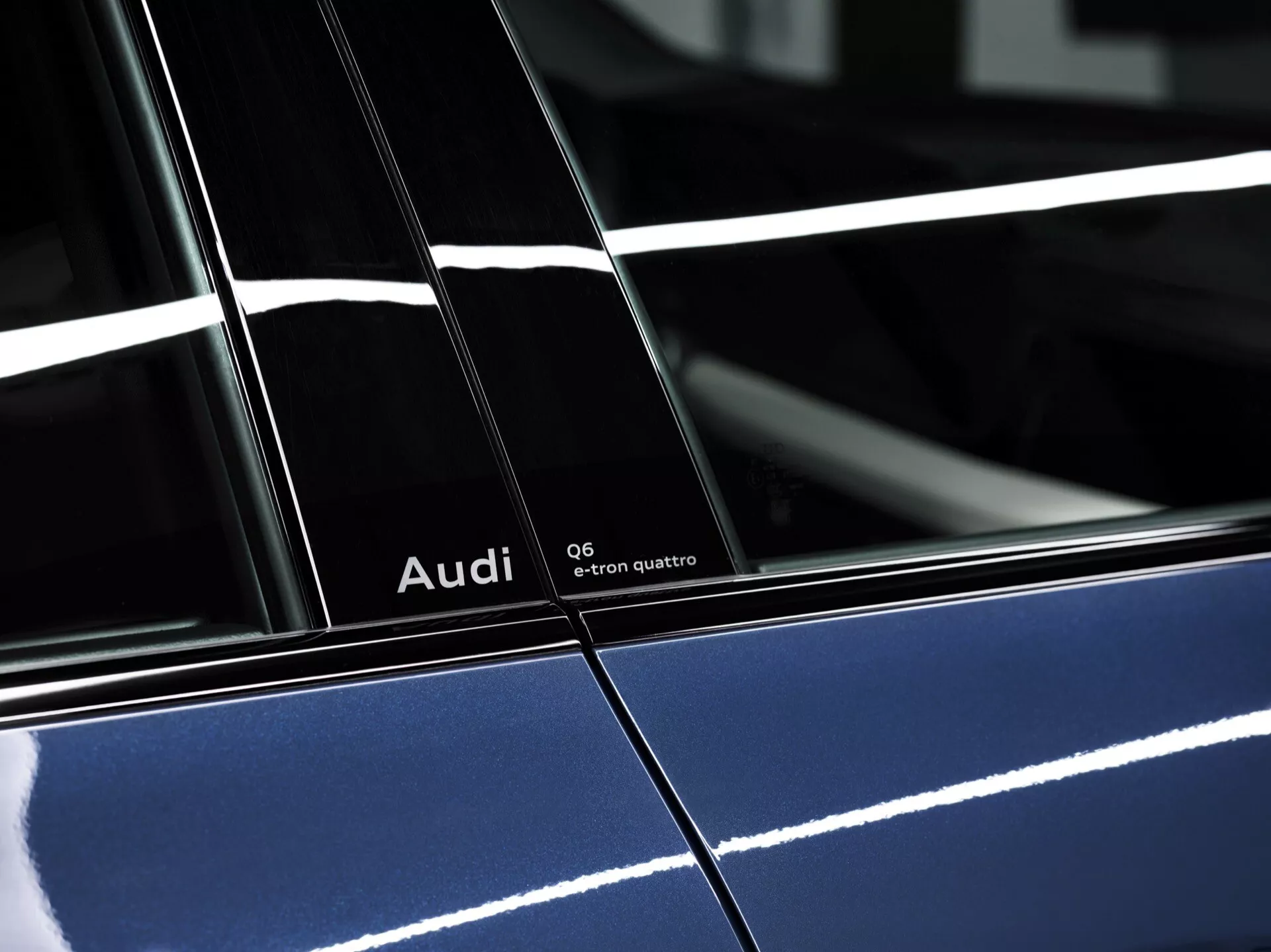 Vysoce kvalitní boční profil 2024 Audi Q6-e-tron quattro v hluboké modré barvě s lesklým finišem, znázorňující výrazné značení a detaily designu, zvýrazňující B-sloupek mezi dveřmi a odrážející osvětlení.