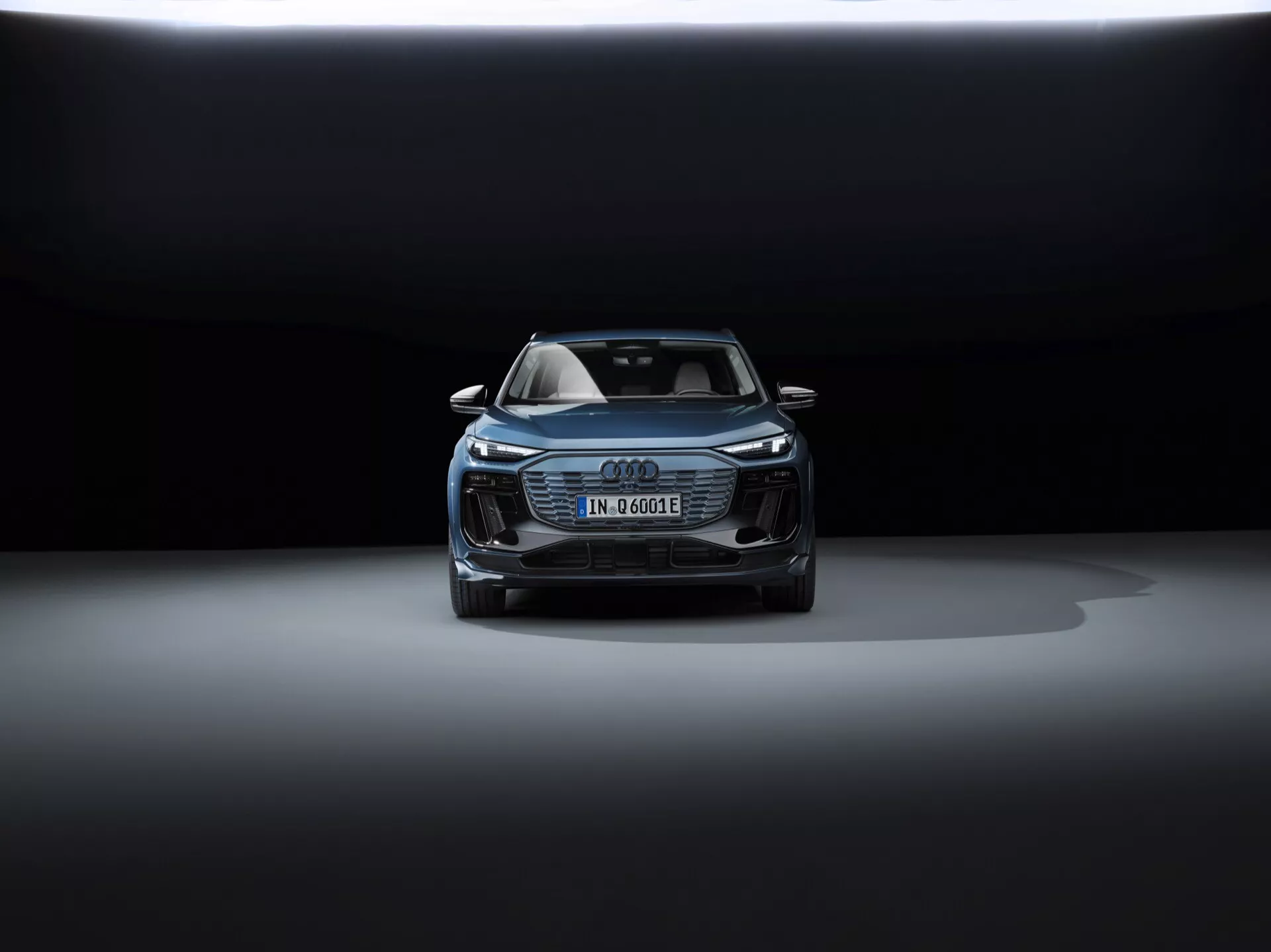 Pohled zepředu na Audi Q6 e-tron 2024, který ukazuje kapotu, masku chladiče, část střechy a přední design. Elegantní světlomety pravděpodobně mají LED technologii. Německá poznávací značka naznačuje elektrický nebo hybridní model. Výrazná maska Audi Singleframe, další otvory a možné bezpečnostní senzory, všechny podtrhují jeho pokročilé asistenční technologie. Dramatické osvětlení s tmavým pozadím a nasvícení shora zvýrazňují luxusní a sofistikovaný design vozu.
