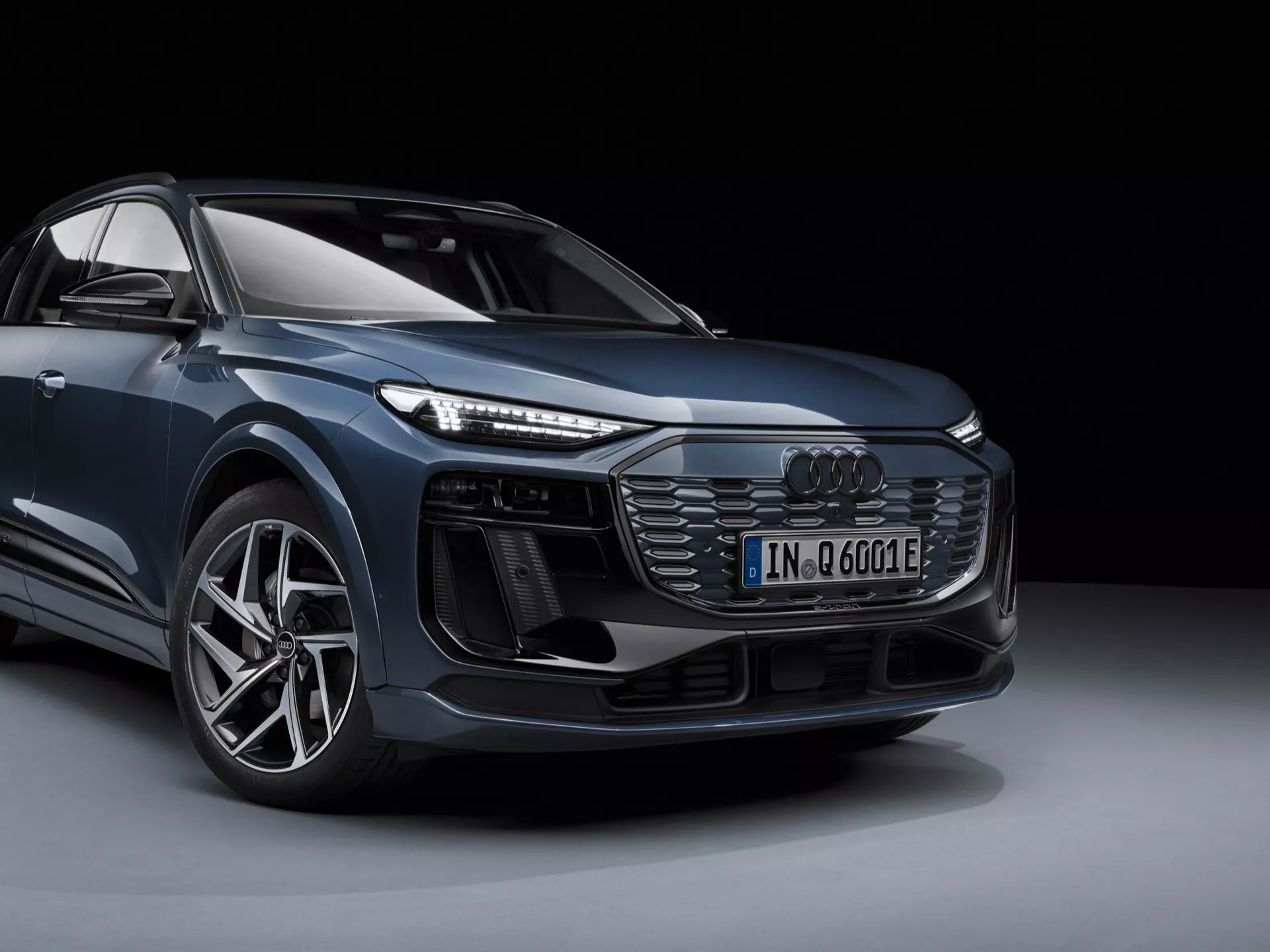 Luxusní SUV Audi Q6 e-tron 2024 fotografováno z nízkého tříčtvrtečního úhlu zepředu, zobrazující elegantní kovové linie karoserie, velká slitinová kola, výrazné LED světlomety a dominantní přední mřížku na tmavém pozadí.