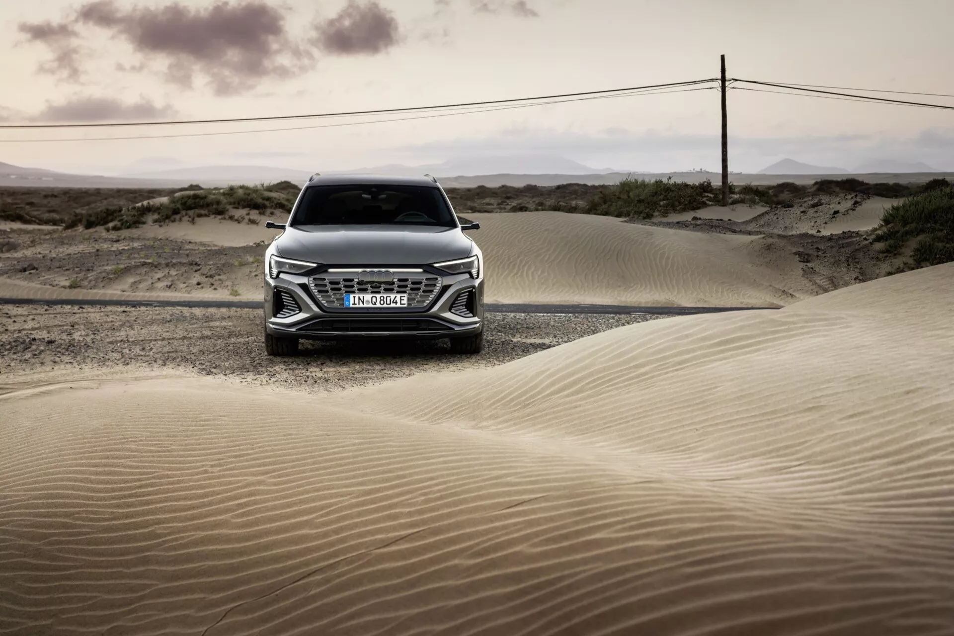 Čelní pohled na Audi Q8 e-tron 2023 v krajině pouště za svítání nebo soumraku, zdůrazňující jeho mřížku, kapotu a pokročilý design světlometů