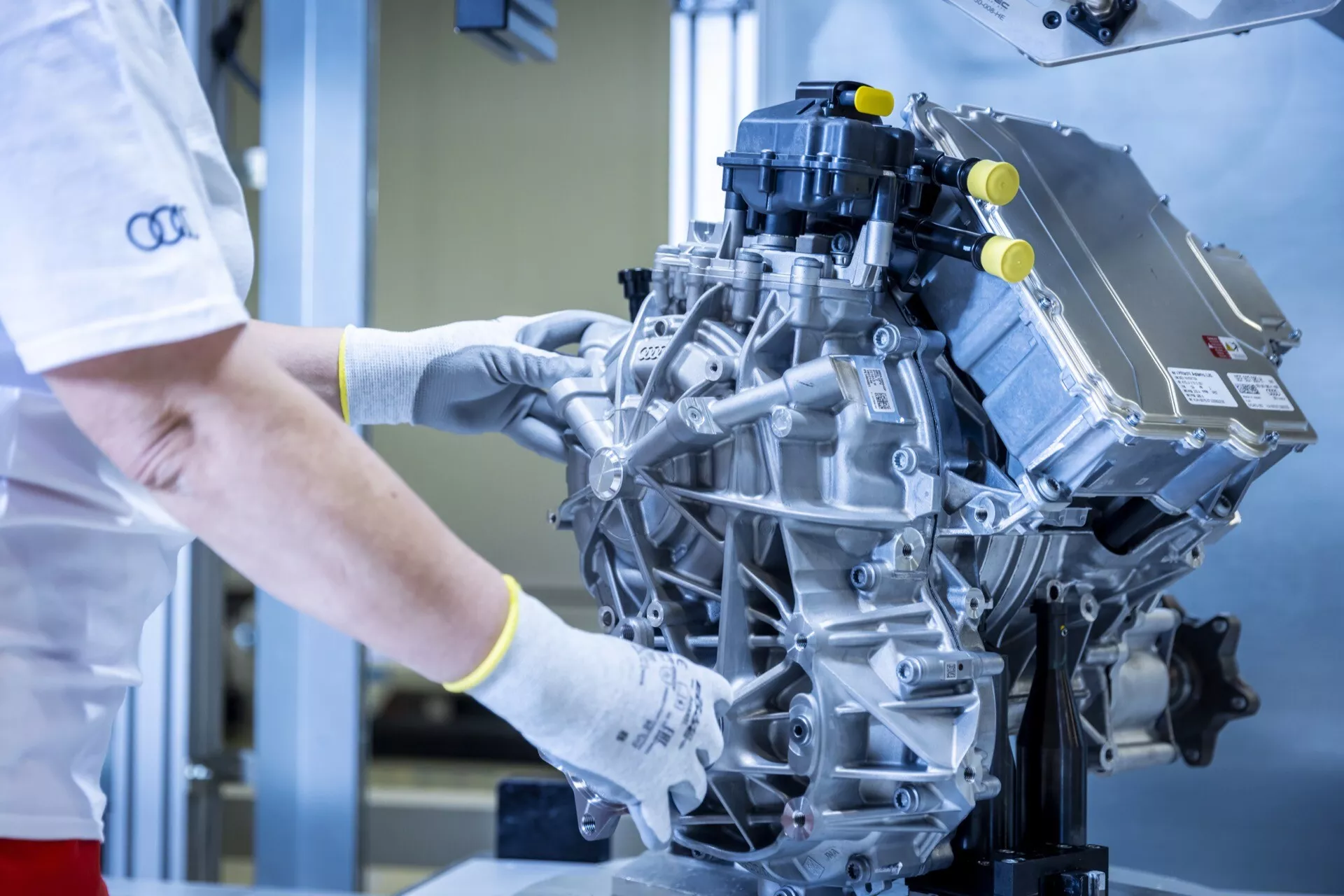 Detailní pohled na moderní výkonný motor s technikem provádějícím kontrolu v čistém průmyslovém prostředí, zvýrazňující komponenty jako je sací potrubí a zapalovací cívky.