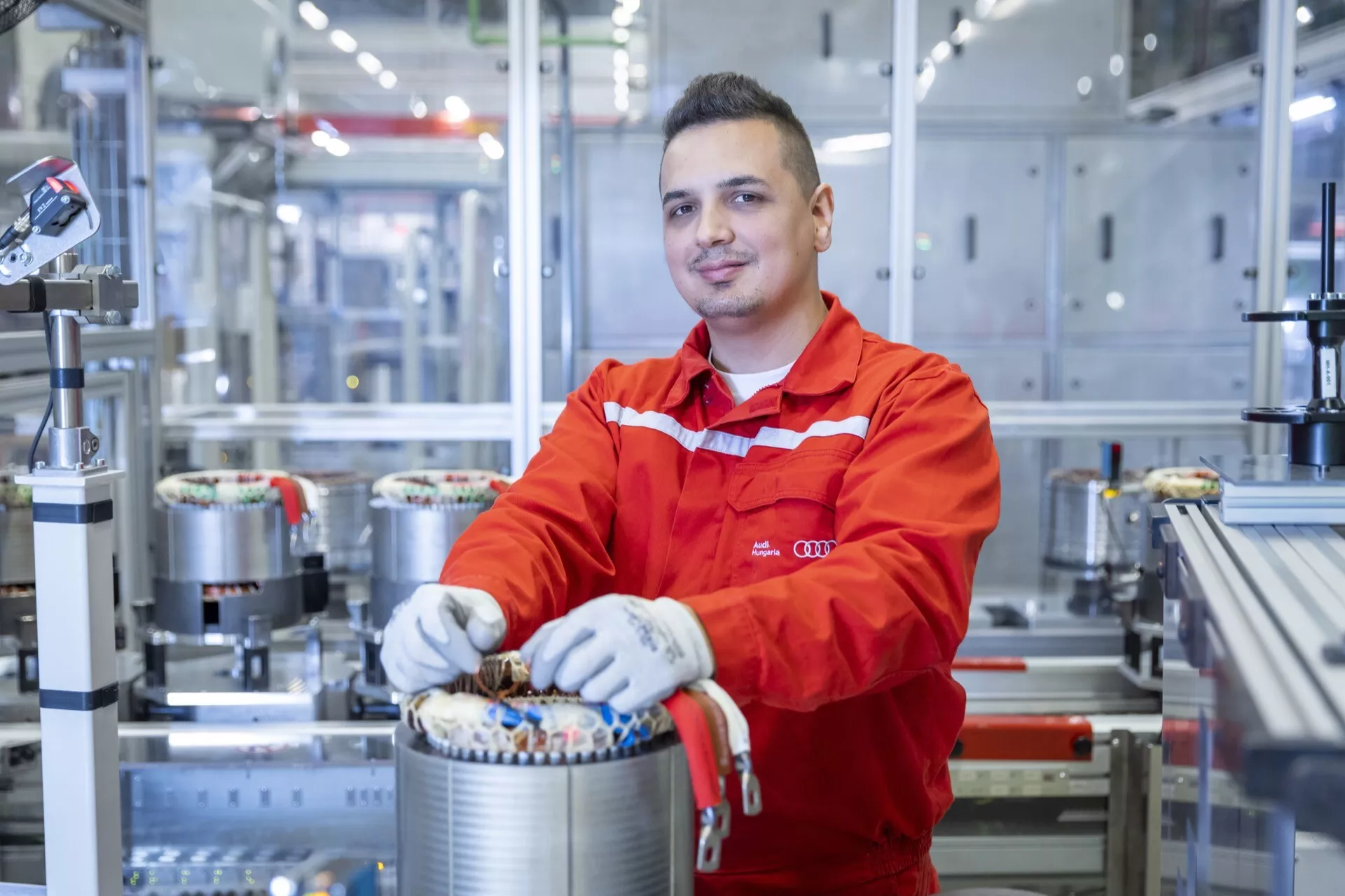 Odborník na automobilové inženýrství v červené uniformě pracuje na komponentu elektrického pohonu ve moderní výrobní závodě