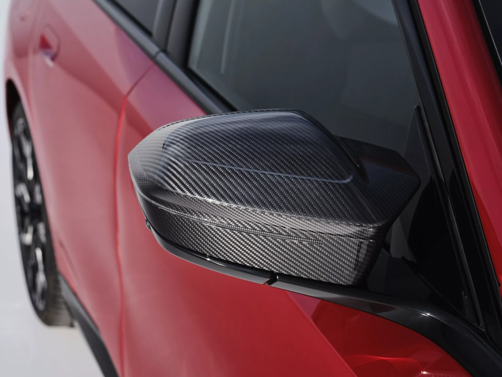 Detailní snímek bočního zrcátka BMW řady 5 (G60-G61) 2023 s obalem z uhlíkových vláken v tmavě červené barvě, zdůrazňující aerodynamický design a technologii materiálů.