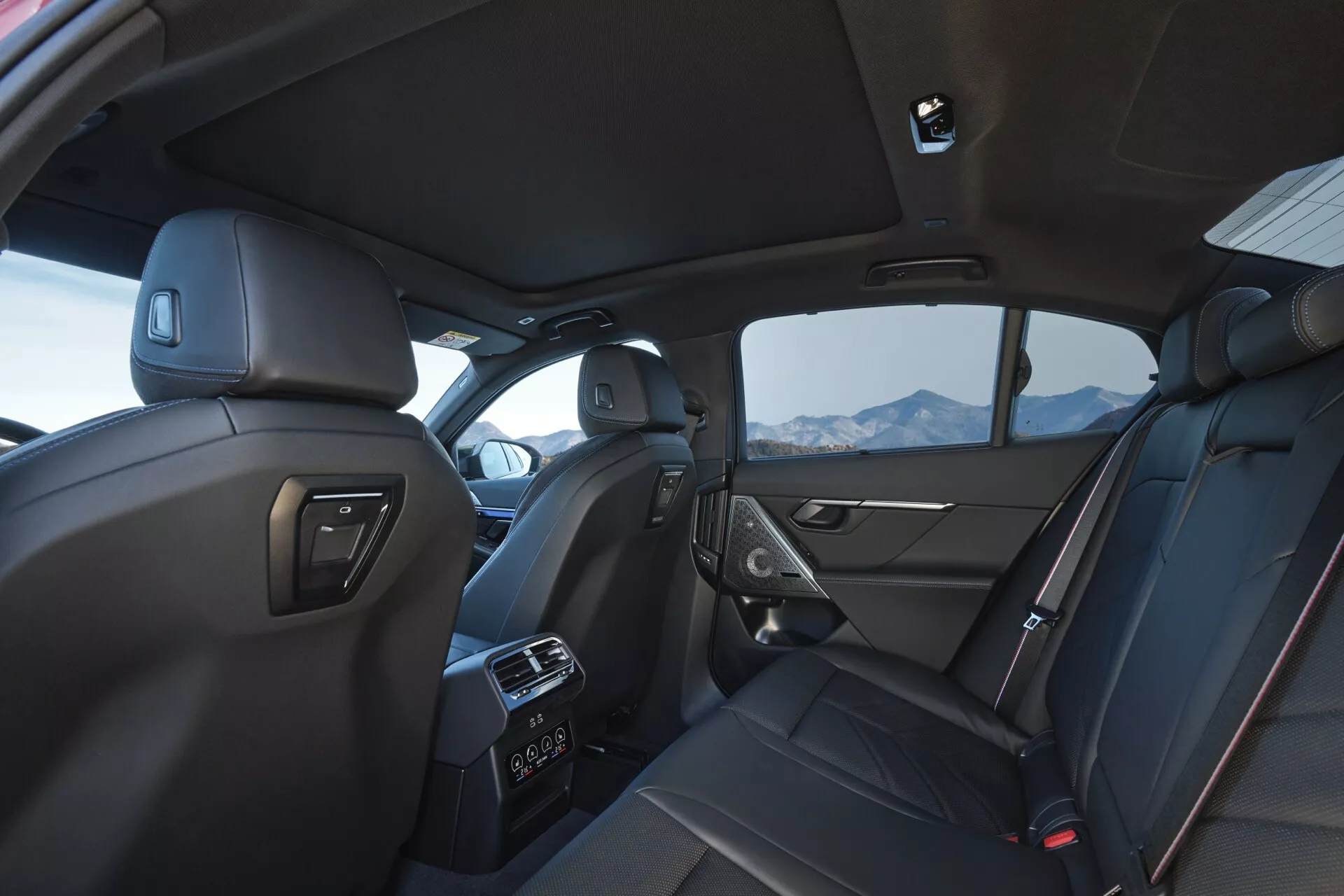 Pohled na interiér BMW řady 5 (G60-G61) z roku 2023 z perspektivy zadního cestujícího, s prvotřídními koženými sedadly, nastavitelným sedadlem spolujezdce s výškově nastavitelným bezpečnostním pásem, kapsou na zadní straně sedadla, ovládáním elektrických oken, reproduktorem na dveřích spolujezdce, rukojetěmi na stropě, stropním světlem a vestavěným mikrofonem, ventilačními otvory klimatizace pro zadní pasažéry, kapacitou pro pět cestujících s ukotvením bezpečnostních pásů a ukotveními ISOFIX/LATCH pro dětské autosedačky.