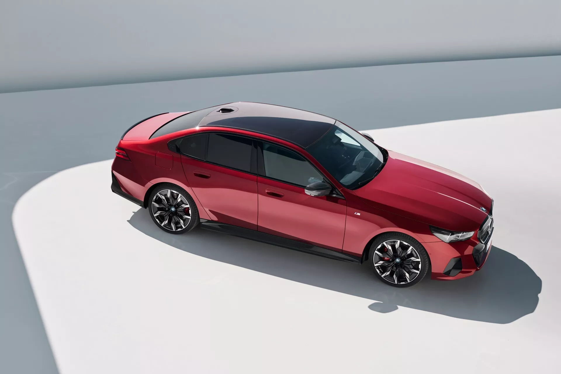 Pohled shora pod úhlem na BMW řady 5 z roku 2023 (G60-G61) zobrazující horní a boční profil, s aerodynamickým designem, lesklými slitinovými koly, střešním oknem a pokročilou světelnou technologií.