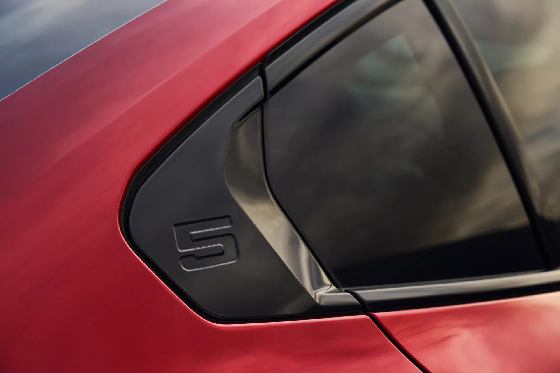 Detailní záběr na červený vůz BMW řady 5 (G60-G61) se zaměřením na oblast C-sloupku s výrazným trojúhelníkovým oknem a elegantním designem karoserie