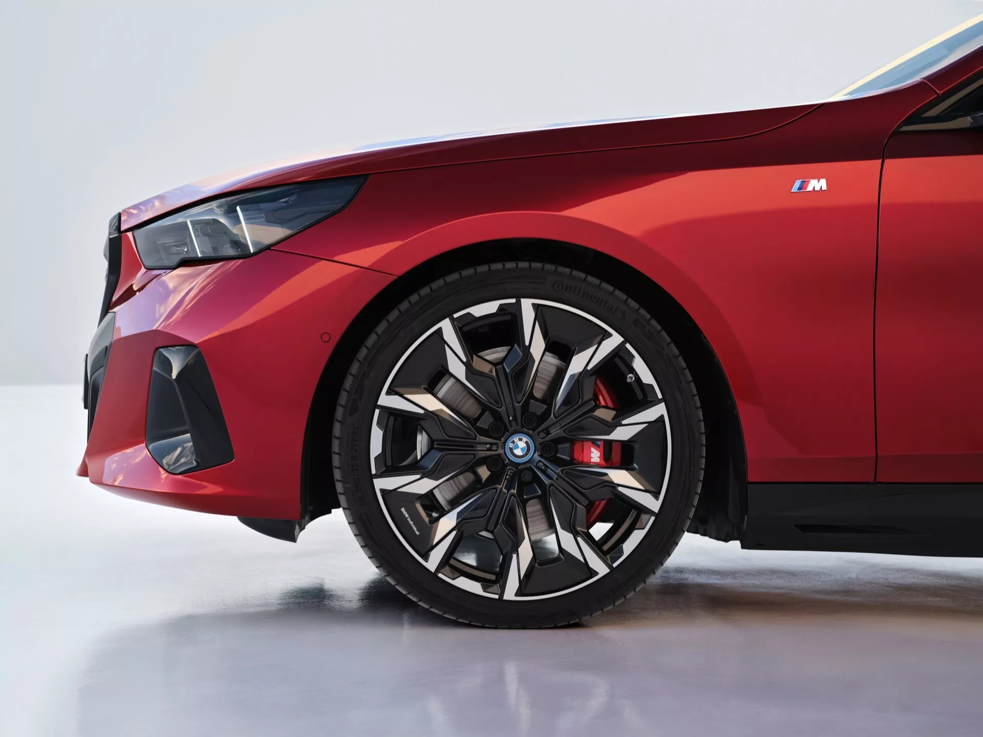 Detailní pohled na přední levou stranu BMW řady 5 (G60-G61) rok 2023 s koly a blatníkem, včetně detailů jako logo na modrém středovém krytu, červený brzdový třmen a přední nárazník orientovaný na výkon.