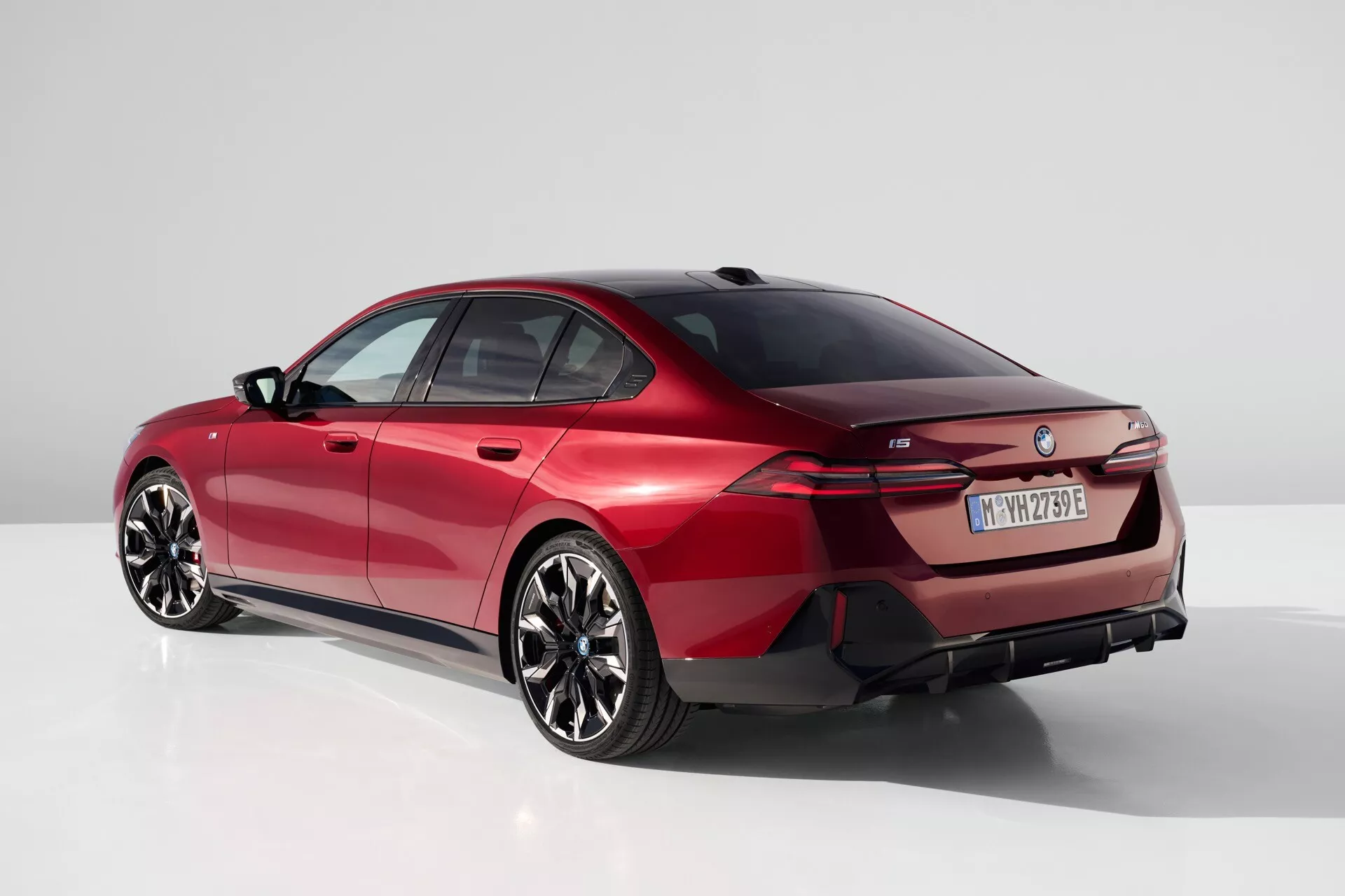 Moderní sedan BMW řady 5 (G60-G61) roku 2023 ve studiu, pohled ze zadního tříčtvrtečního úhlu zdůrazňující elegantní linii střechy, výrazná zadní světla a sportovní aerodynamický profil v jasně červené barvě