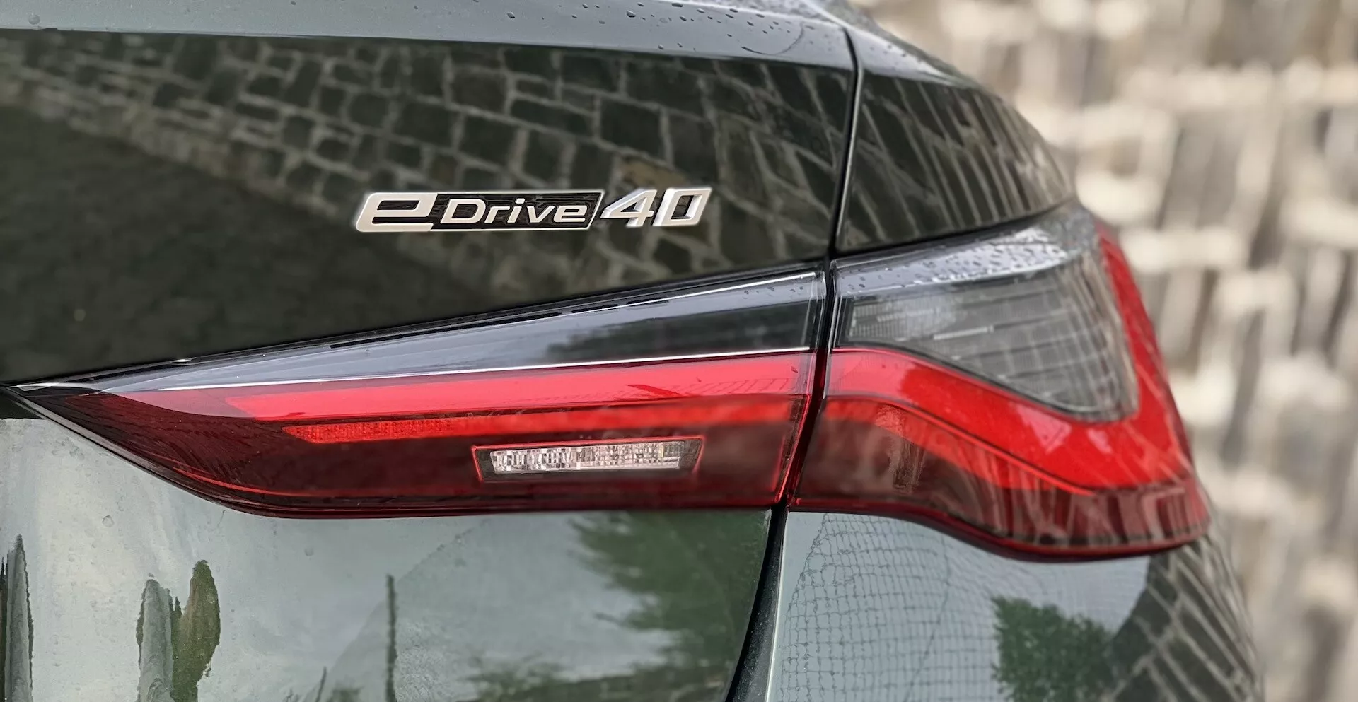 Detailní pohled na zadní roh BMW i4 2021 s důrazem na zadní světlo a označení eDrive 40 s technologií LED a odrazivým lakem.