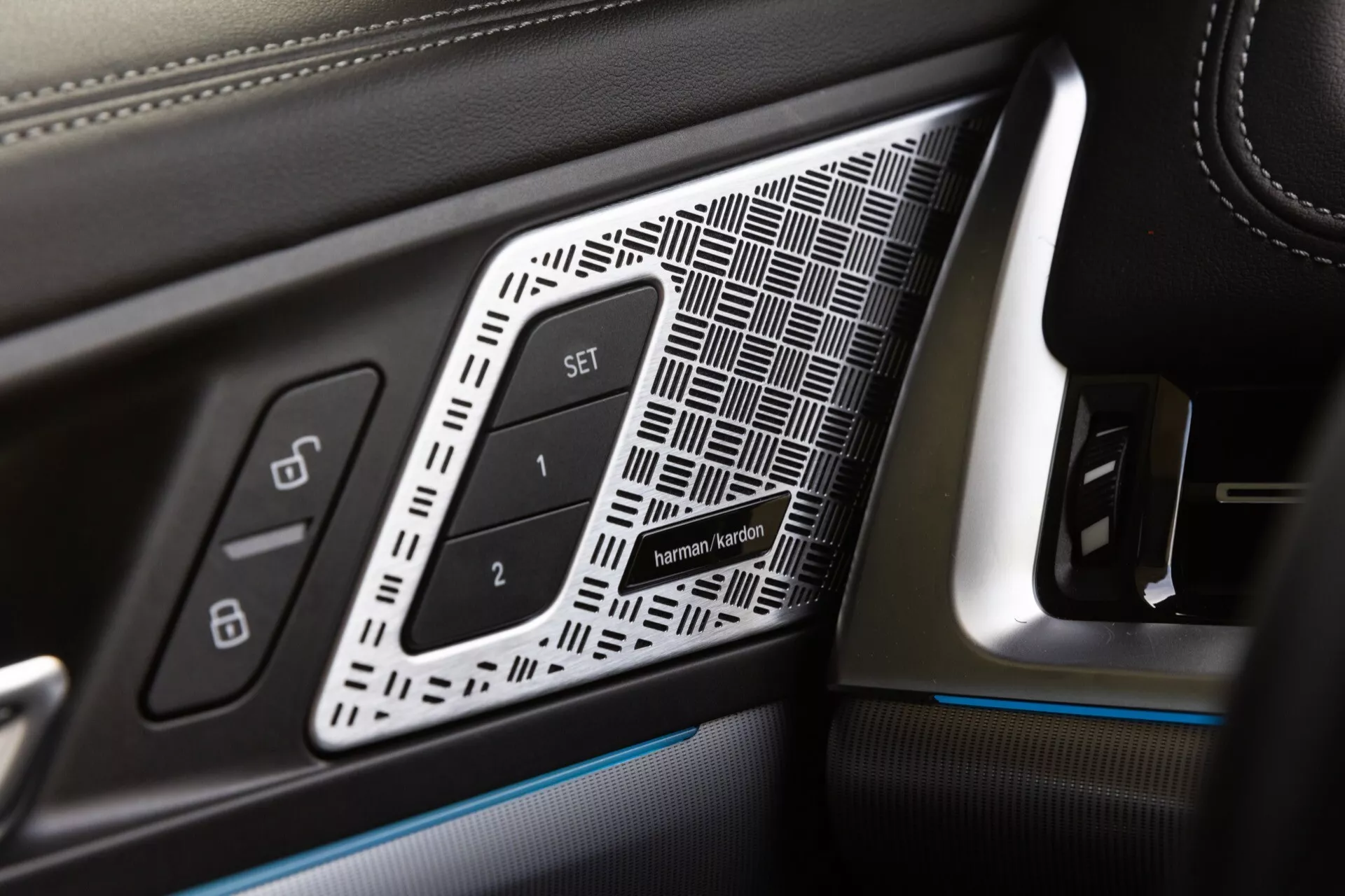 Detailní pohled na panel dveří řidiče v BMW X1 roku 2022 (U11) s luxusními prvky jako kůže se zřetelným prošíváním, geometrickou vložkou, tlačítky pro nastavení sedadla a ambientním osvětlením