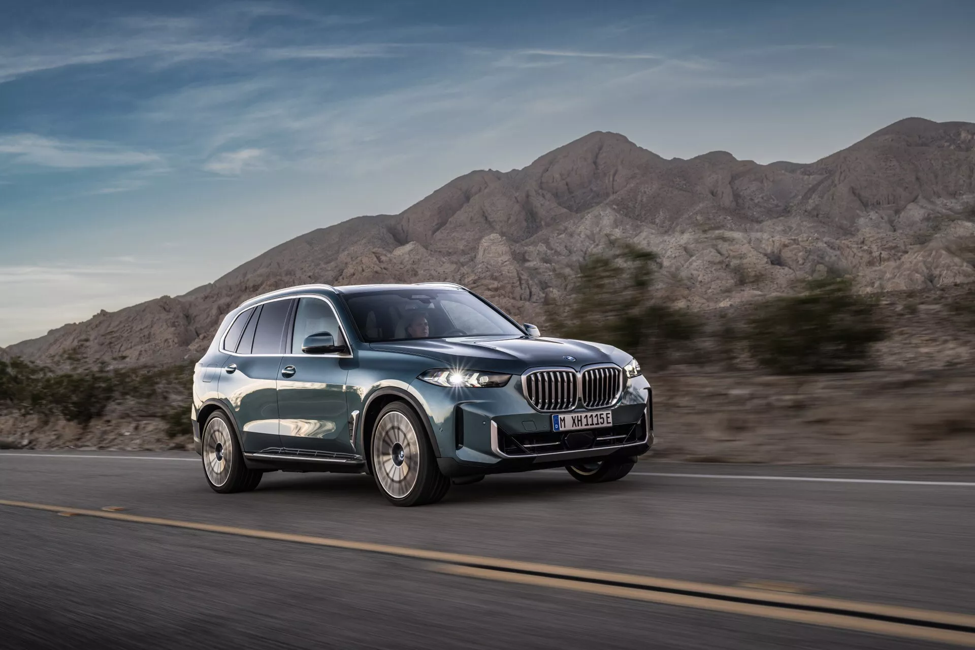 Moderní luxusní SUV BMW X5 2023 (G05-F95 Facelift) v pohybu z úhlu čelního tříčtvrtečního pohledu zdůrazňující dynamický design, velkou ledvinovitou mřížku, úzká LED světlomety, slitinová kola s vícepaprskovým designem a hladký siluetu s metalickým lakem