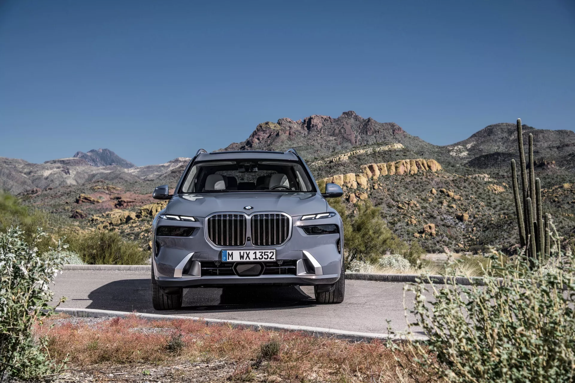 Luxusní SUV BMW X7 2022 (G07-facelift), zobrazující moderní design s velkou ledvinovitou mřížkou, úzkými LED světlomety, pokročilým předním nárazníkem s funkcemi ADAS, tvarovanou kapotou a slitinovými koly, dominantně parkované na silnici na pozadí pouště a hor pod čistě modrou oblohou