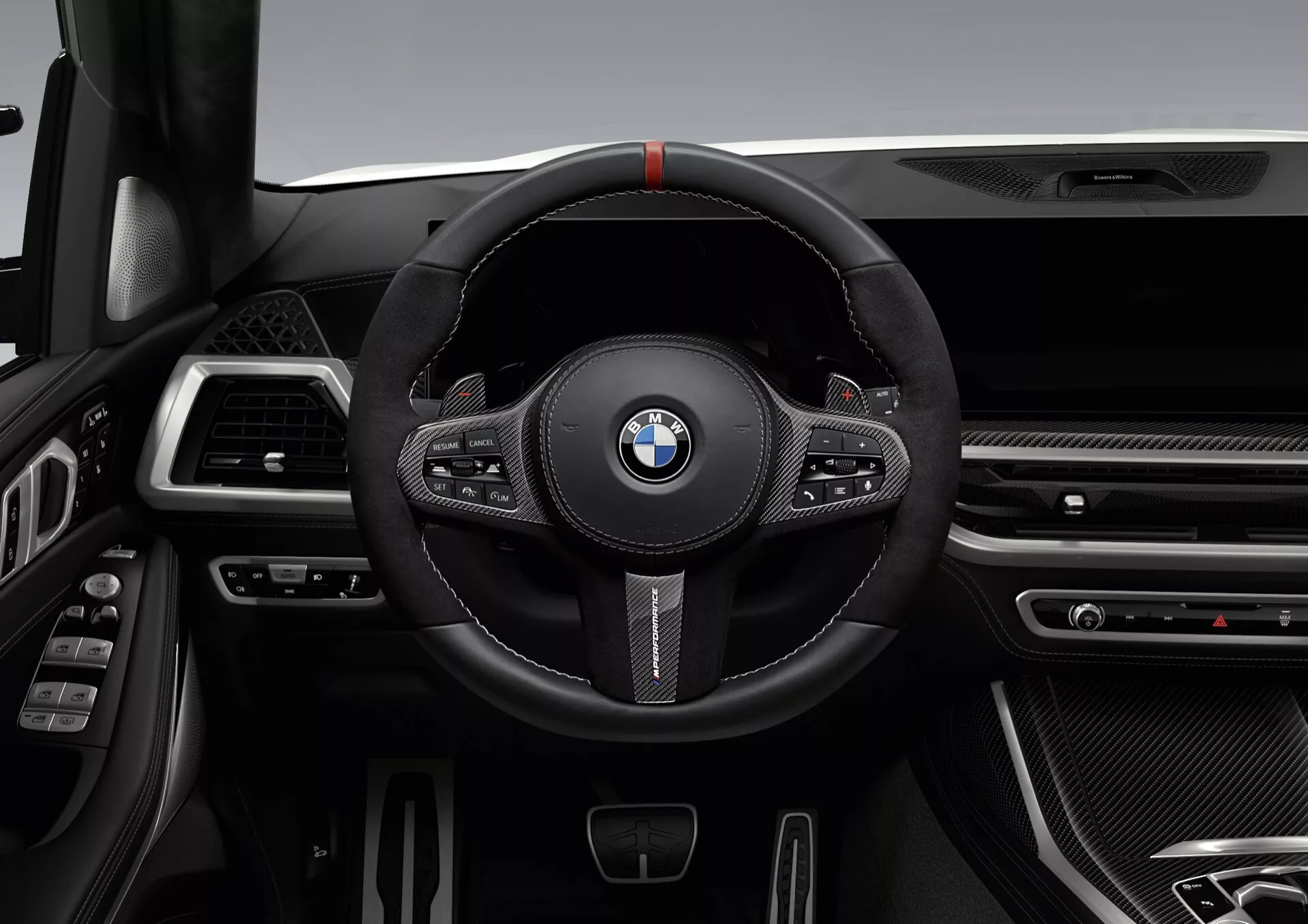 Interiér BMW X7 2022 (G07-Facelift) s důrazem na sportovní volant potažený černou kůží se červeným značením, multifunkčními tlačítky a pádly pro manuální řazení proti sofistikované palubní desce se štíhlými ventilačními otvory, chromovými a texturami podobnými uhlíkovým vláknům