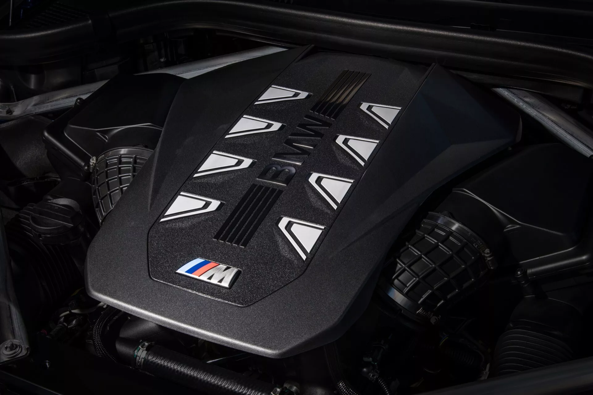 Detailní pohled na kryt výkonného motoru v BMW X7 2022 (G07-Facelift) s emblémem M, který předvádí pokročilé designové prvky a otvory pro chlazení