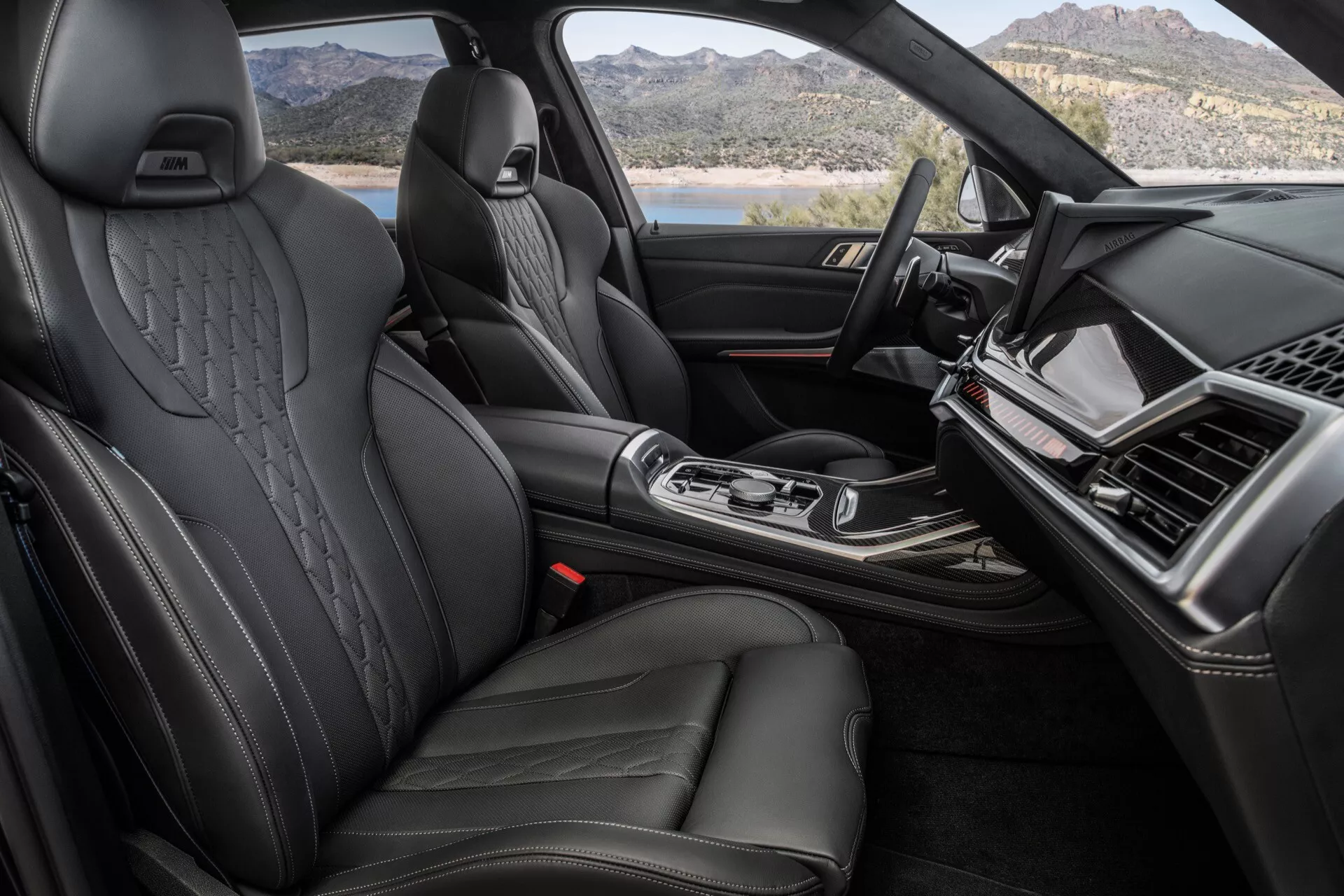 Interiérový pohled na BMW X7 2022 (G07-Facelift) se zaměřením na prémiovou přední kabinu s černými koženými sedadly s bočními opěrkami a reliéfními opěrkami hlavy, elegantní palubní deska s obrazovkou infotainmentu, centrální konzola s ergonomickou pákou řazení a vysoce kvalitními povrchy naznačujícími luxusní vozidlo.