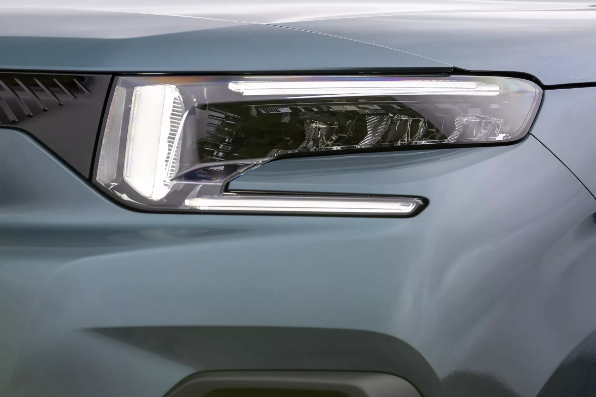 Detailní snímek předního rohu Citroen Berlingo 2024 s moderním designem LED světlometu, LED denního svícení, sekundárním osvětlením a aerodynamickou karoserií v modro-šedé barvě