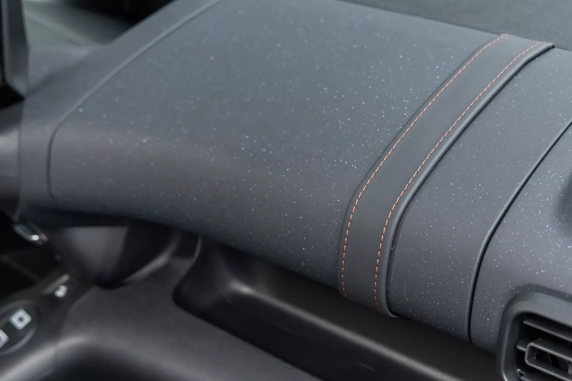 Detailní pohled na palubní desku Citroen Berlingo 2024 (facelift 3. generace) se zobrazením texturovaného tmavého materiálu s kontrastním červeným prošíváním, bez viditelných technologických prvků