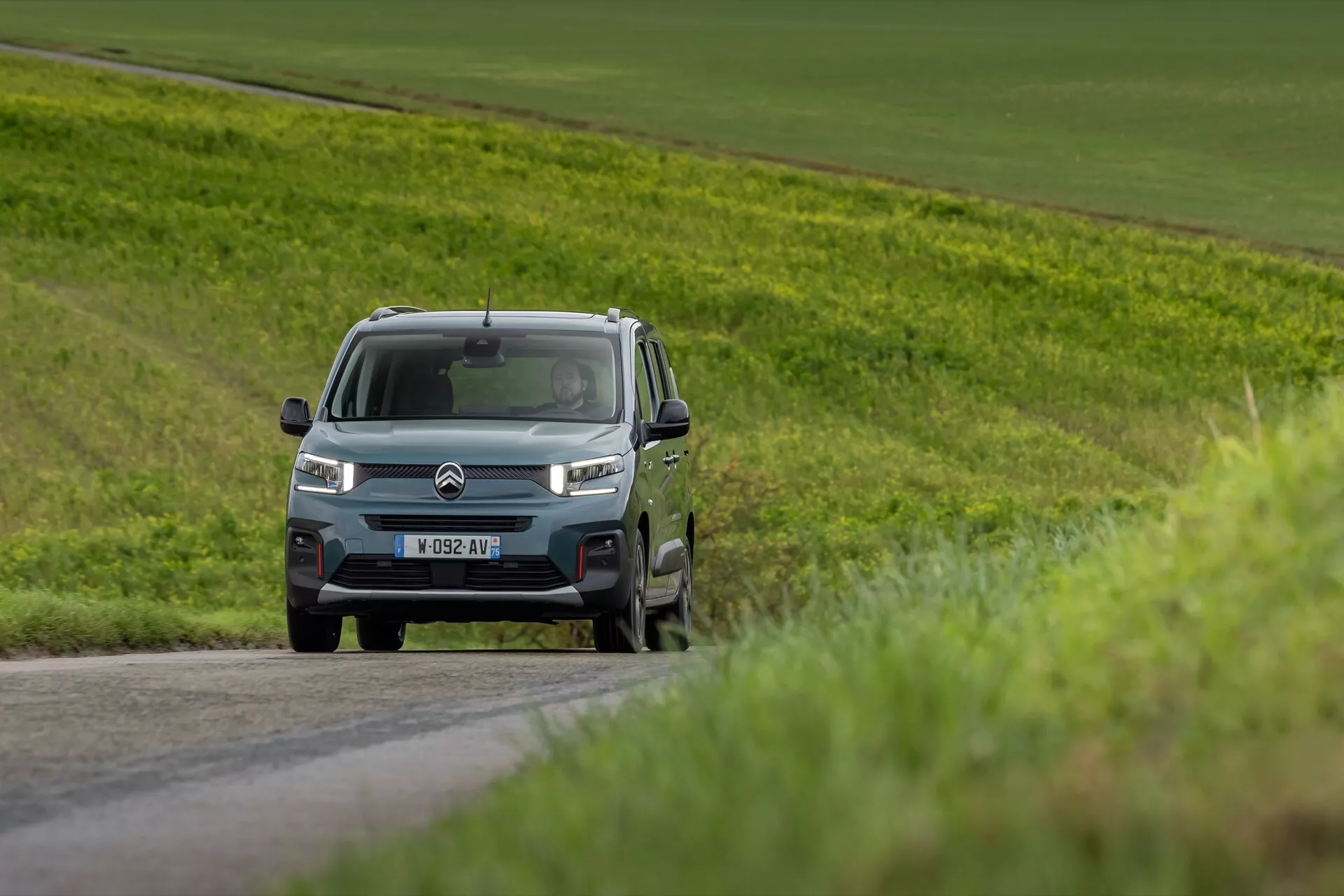 Faceliftový model Citroen Berlingo 2024 jedoucí po venkovské silnici, předvádějící přední mřížku, LED světlomety a boční profil