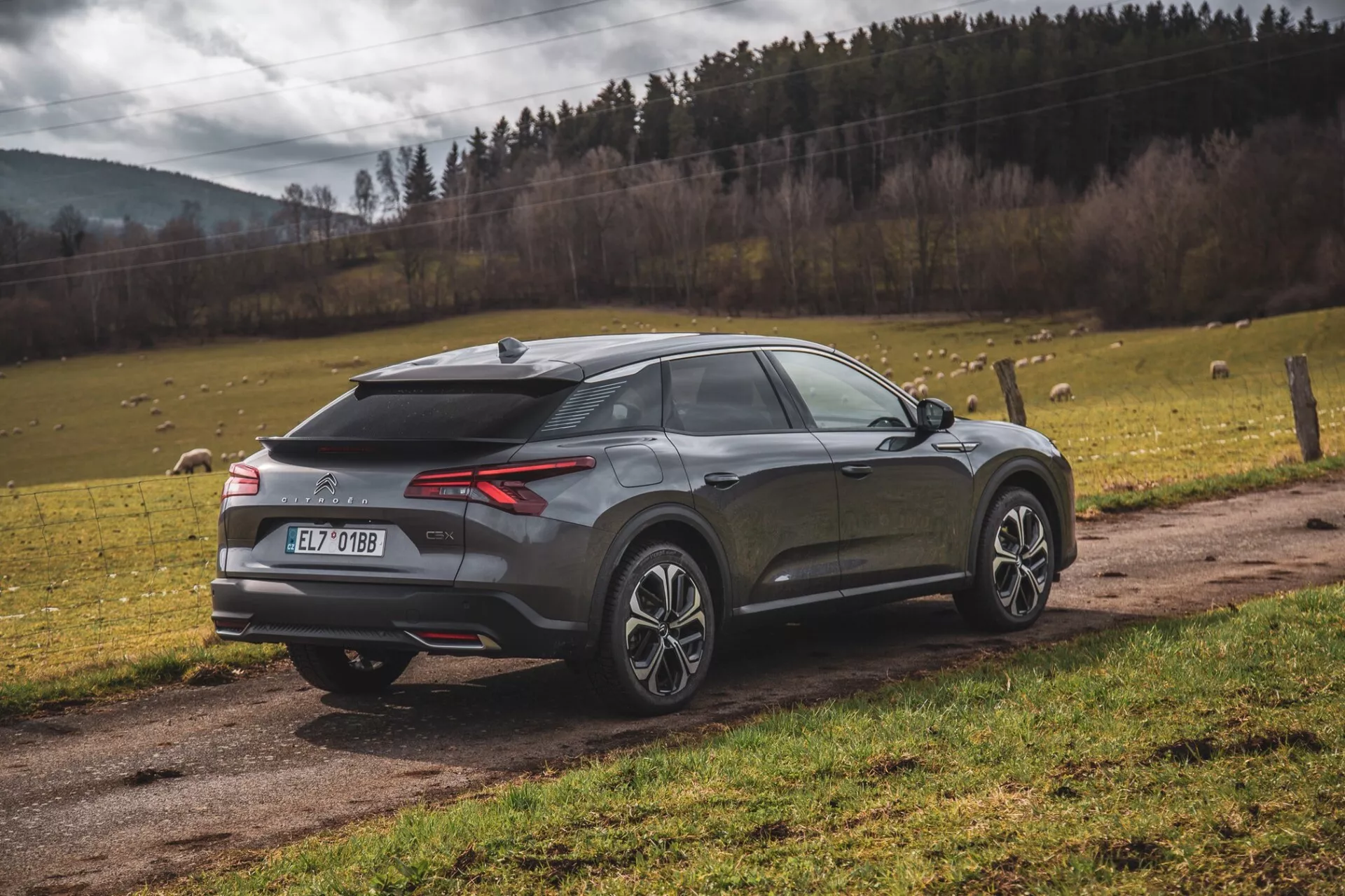 Moderní crossover SUV Citroen C5-X 2022 zaparkovaný venku, pohled na zadní tři čtvrtiny zdůrazňující LED zadní světla, zadní difuzor, senzory parkování nebo kameru, anténu ve tvaru žraločí ploutve, dvoubarevná slitinová kola, skloněné zadní okno, integrované křídlo a metalický lak na pozadí přírodní krajiny