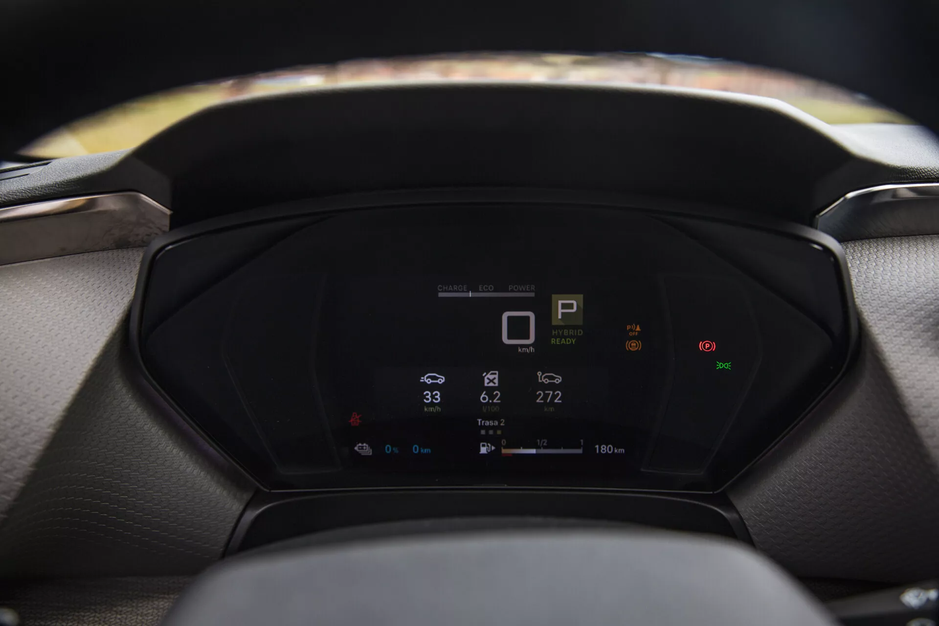 Detailní pohled na digitální palubní desku Citroen C5-X 2022 zobrazující metriky vozidla včetně indikátoru převodovky, tachometru a spotřeby energie, s rozmazaným volantem a čelním sklem v popředí a pozadí.