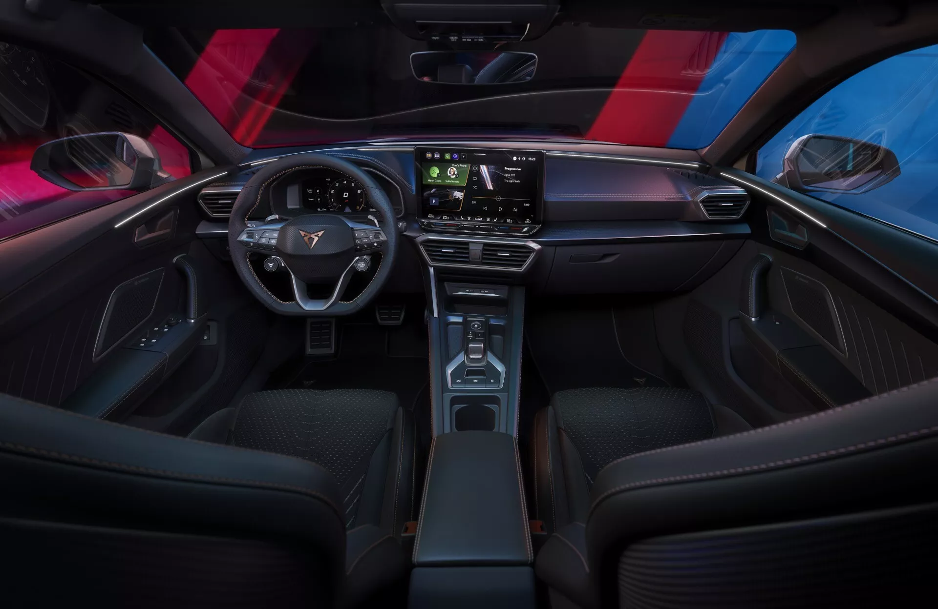 Interiérový záběr na Cupra Leon 2024 (facelift 1. generace) z pohledu zadního sedadla, který ukazuje elegantní, minimalistickou palubní desku s velkým dotykovým displejem, moderní dvouramenný volant s ovládacími prvky a úzkou středovou konzolu s dřevěným dekorem. Sportovní přední sedadla, ambientní osvětlení a panoramatická střecha zdůrazňují sofistikovanou, technologicky pokročilou atmosféru kabiny.