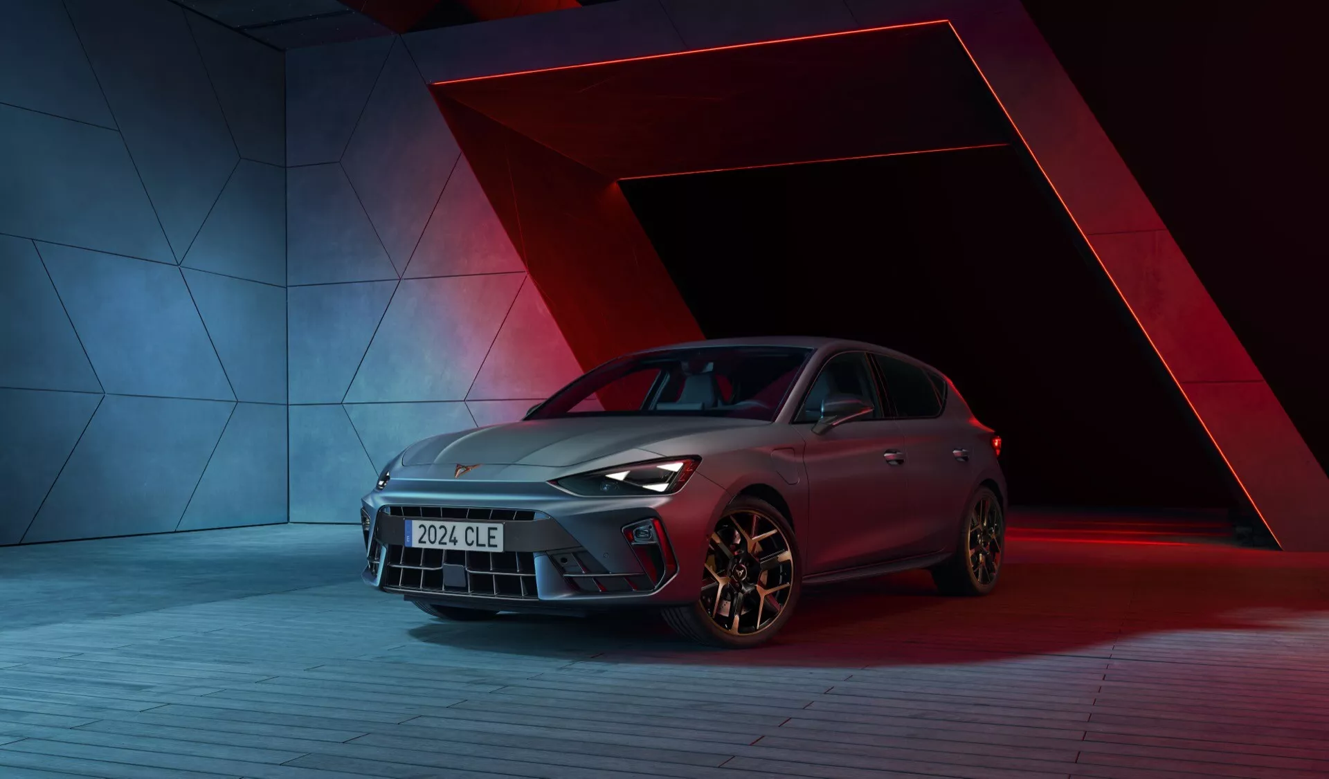 Obrázek kupé Cupra Leon 2024 (1. generace facelift) v dynamickém studiovém prostředí s výjimečně výrazným červeným a modrým pozadím. Auto je zachyceno z nízkého předního třičtvrtinového úhlu, ukazuje jeho přední mřížku, LED světlomety, slitinová kola, aerodynamický design, pokročilou povrchovou úpravu laku a výrazné kliky dveří. Kompozice a osvětlení zdůrazňují elegantní tvar karoserie a designové prvky vozu.