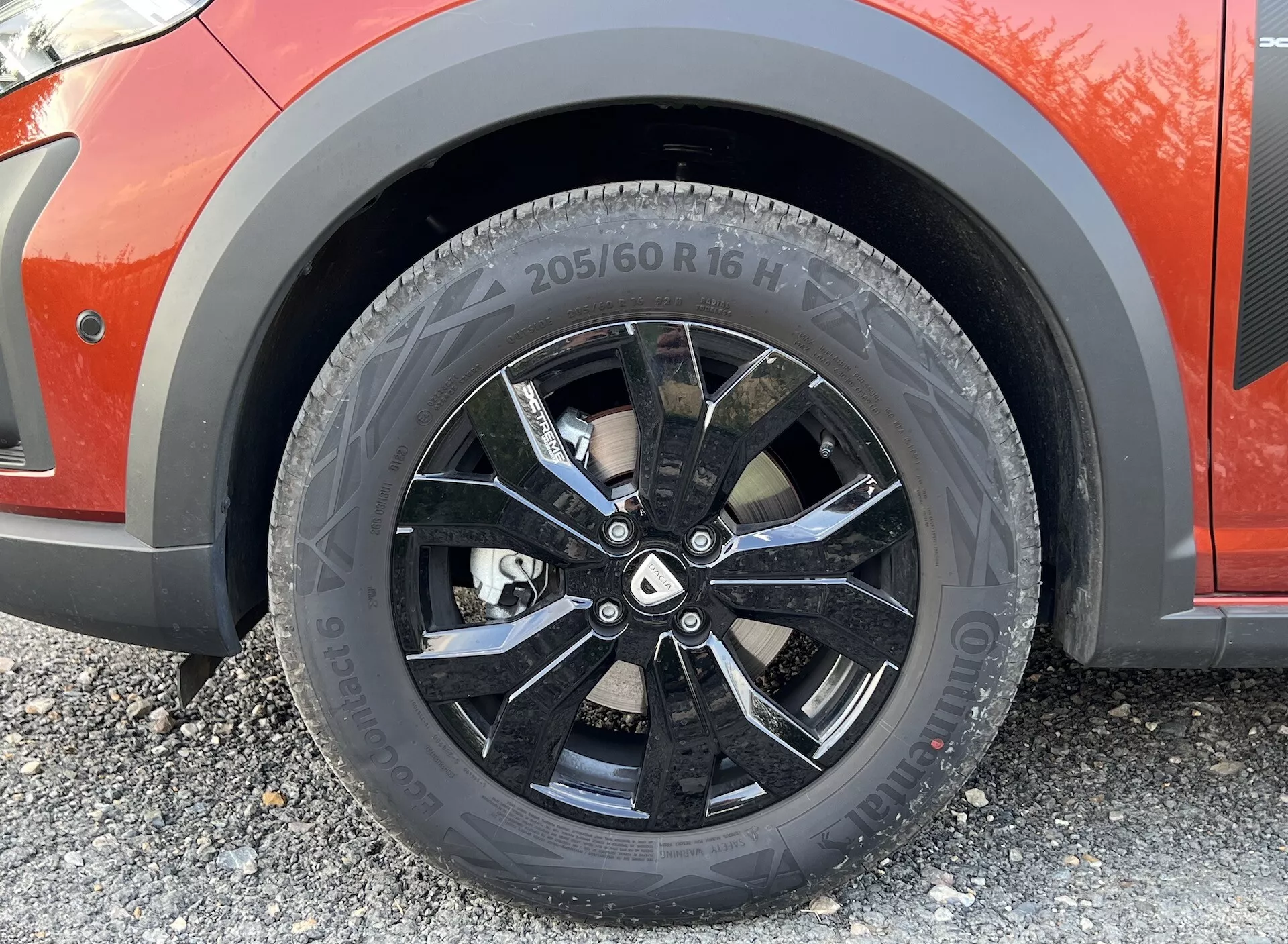 Detailní záběr na přední kolo na straně spolujezdce Dacia Jogger 2022, předvádějící pneumatiku Bridgestone 205/60R16 H, vícepaprskový design kola v lesklé černé barvě a systém kotoučových brzd, zdůrazňující specifikace pneumatiky a kola pro hodnocení technologie a výkonu.