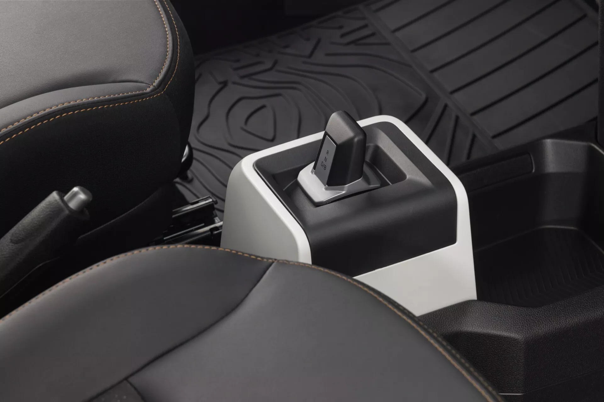 Detailní pohled na interiér Dacia Spring 2024 po prvním faceliftu se zaměřením na elektronický volič převodovky, matně černou středovou konzoli se stříbrnými akcenty, čalouněná kožená přední sedadla a detailně zpracovanou sekci na držáky nápojů z perspektivy mírně nad středovou konzolí, se zaměřením na moderní design a technologické aspekty