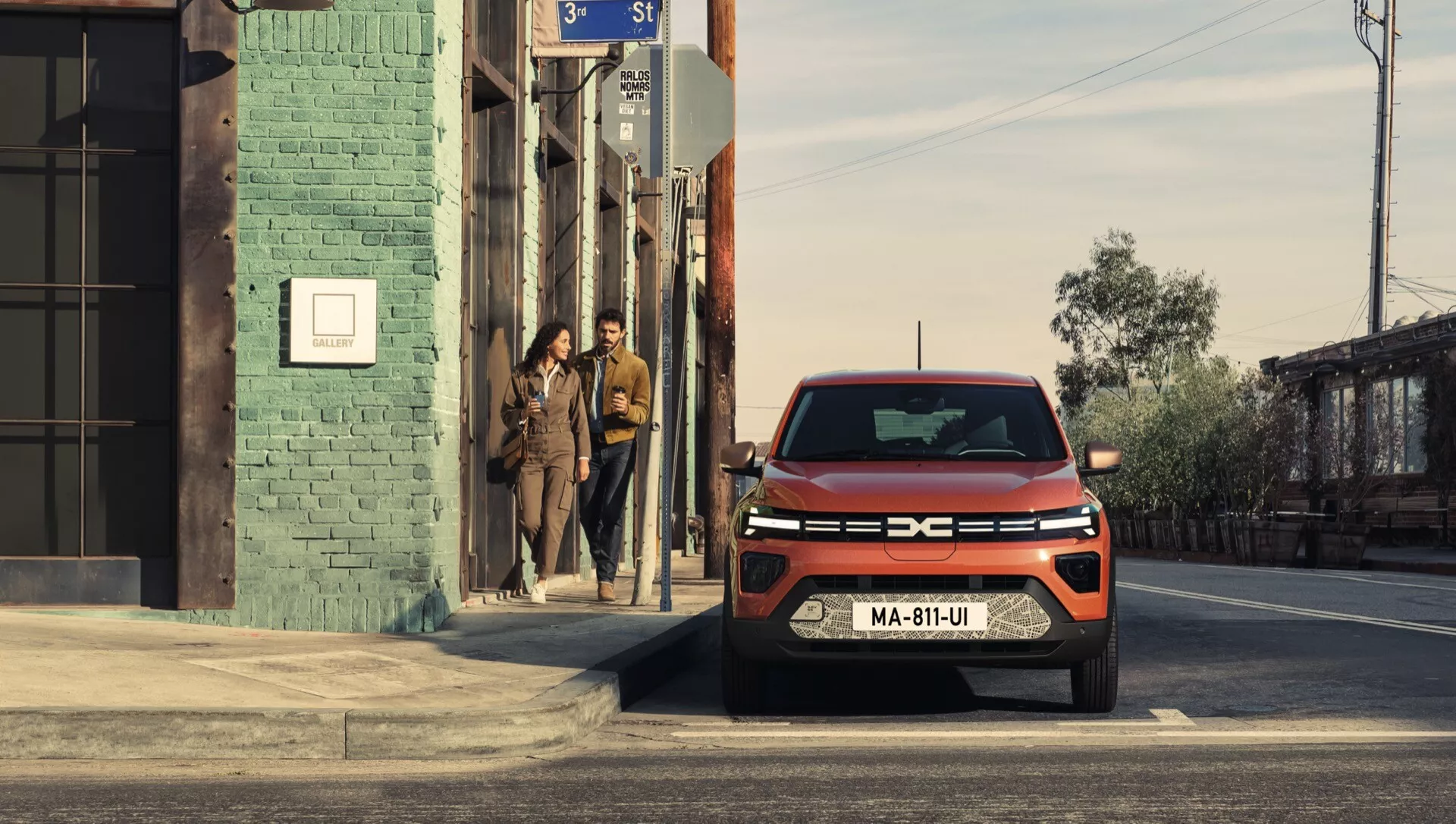 Facelift modelu Dacia Spring 2024 zachycený v městském prostředí, ukazující moderní pohled z předního tříčtvrtečního úhlu s pokročilým LED osvětlením a charakteristickým designem mřížky