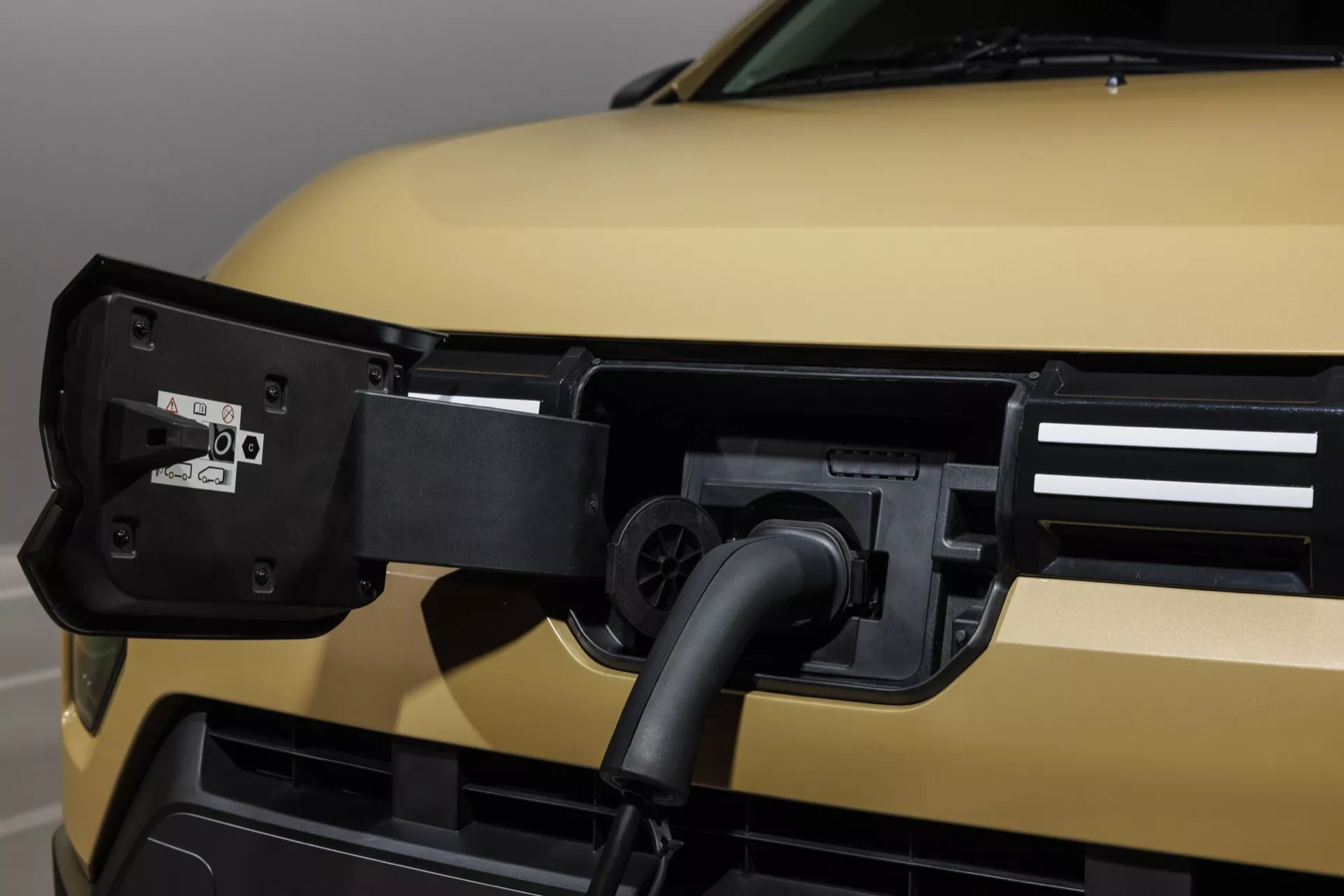 Detailní pohled na přední čtvrtinu Dacia Spring 2024 s důrazem na nabíjecí port pro elektrická vozidla s matně zlatým povrchem