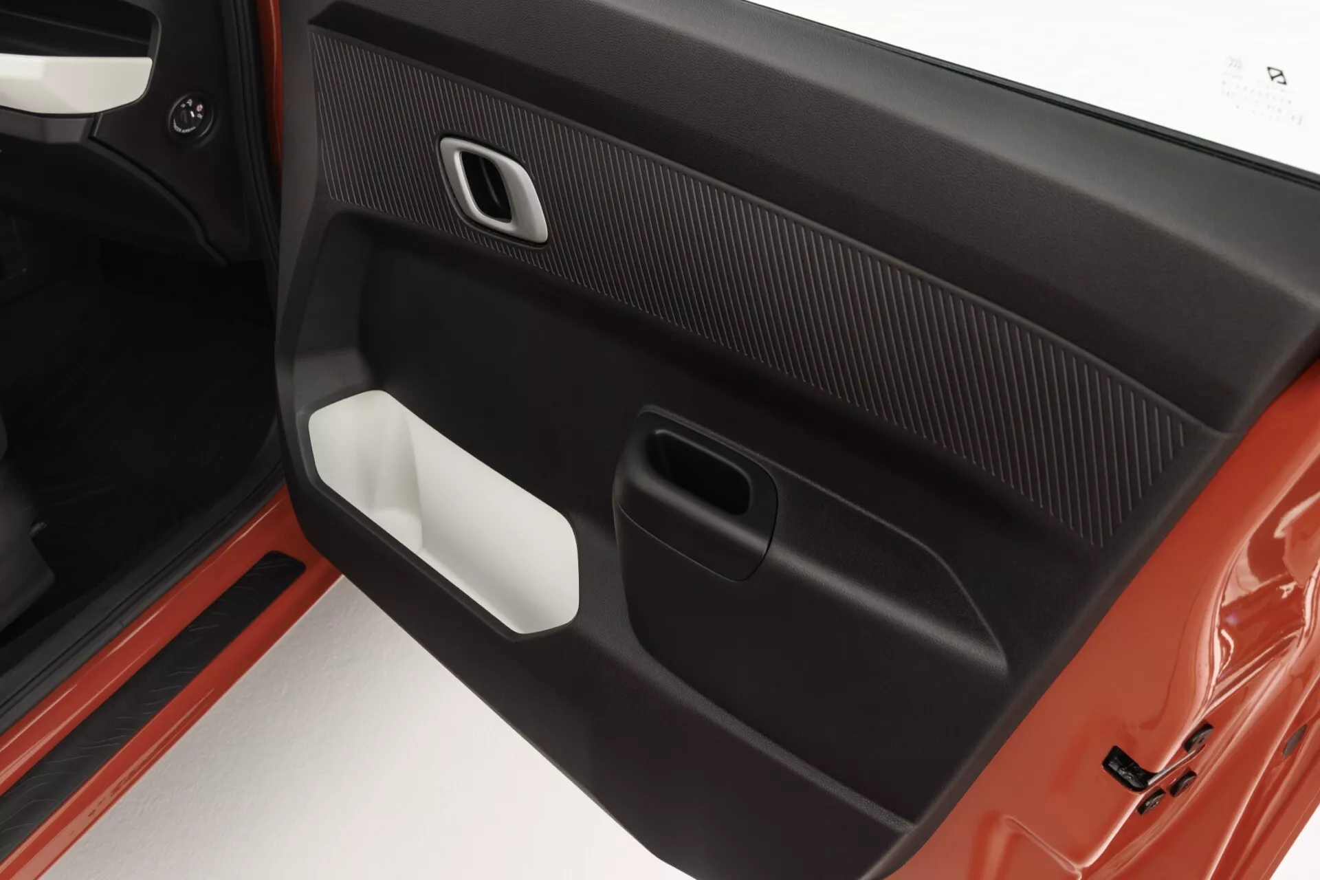 Detailní pohled na vnitřní panel dveří na straně spolujezdce modelu Dacia Spring 2024, předvádějící jeho sofistikovaný design s kombinací materiálů soft-touch a s vzorem uhlíkových vláken, ergonomickou kličku dveří s chromovým povrchem a spodní úložný prostor v barevném schématu dvou odstínů.